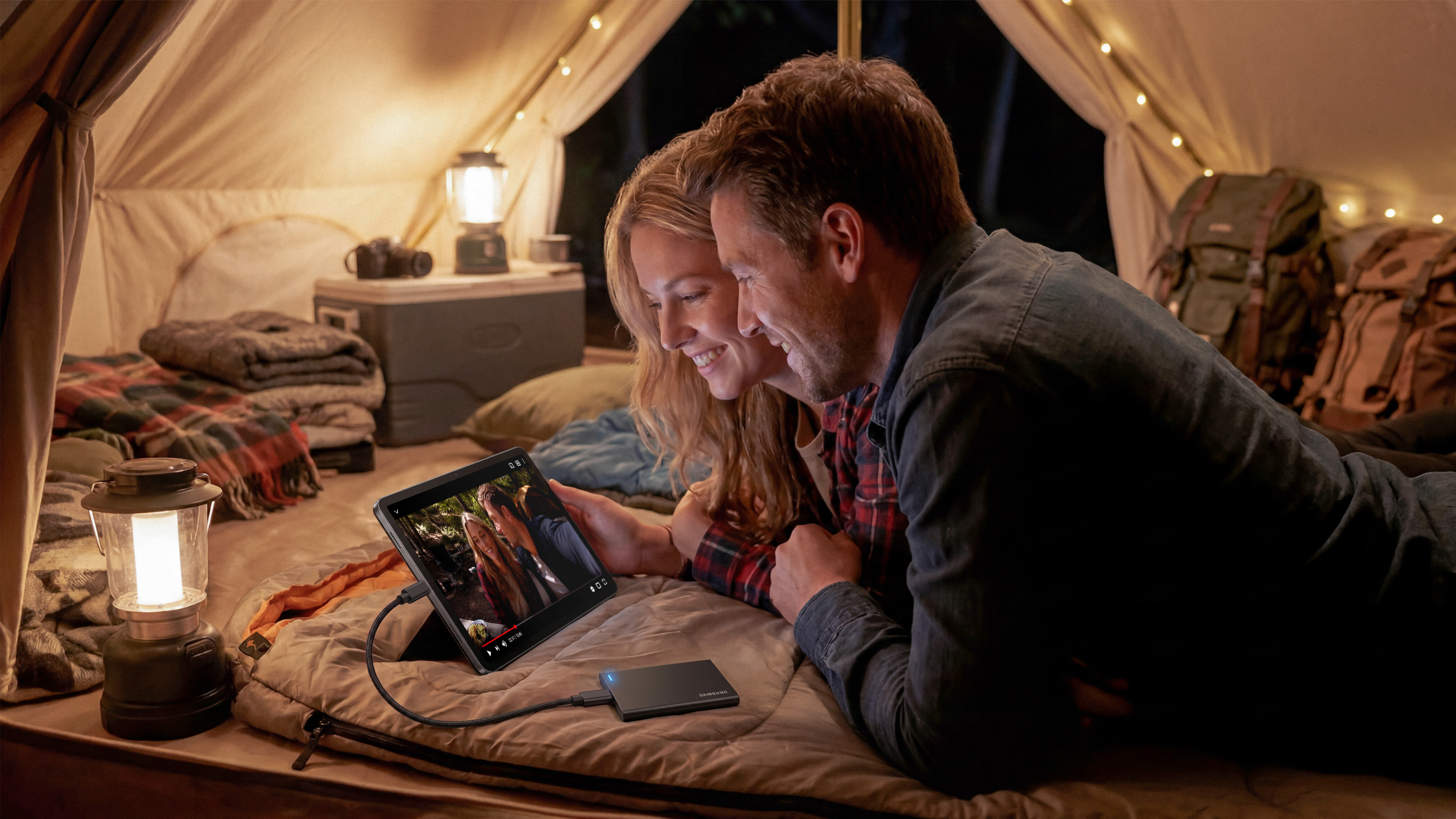 Ein Paar schaut abends gemütlich in einem hell erleuchteten Zelt gemeinsam auf ein Tablet.