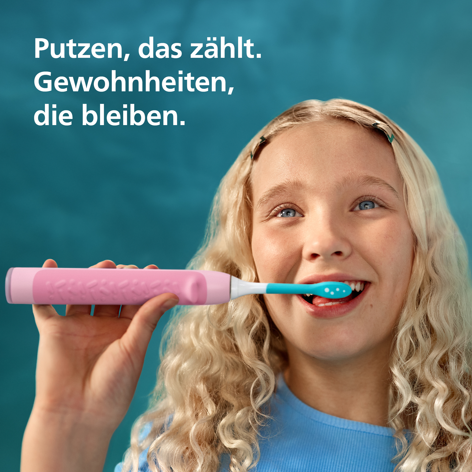 Una ragazza bionda si lava i denti con uno spazzolino elettrico rosa su sfondo blu.