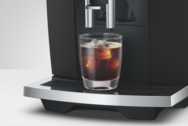 Ein Glas mit Eiskaffee steht auf der Tropfschale einer schwarzen Kaffeemaschine.