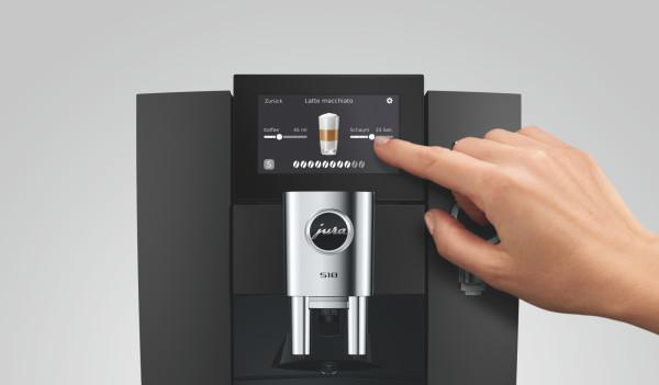 Eine Hand berührt den Touchscreen einer schwarz-silbernen Jura-Kaffeemaschine.