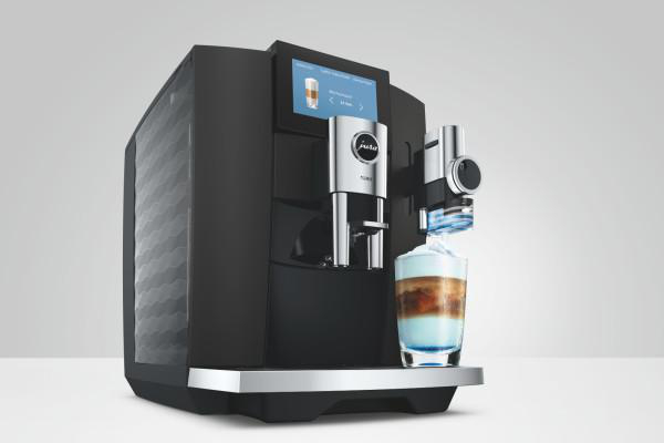Moderne schwarze Kaffeemaschine mit Display und einer frisch gefüllten Tasse Latte Macchiato auf hellem Grund.