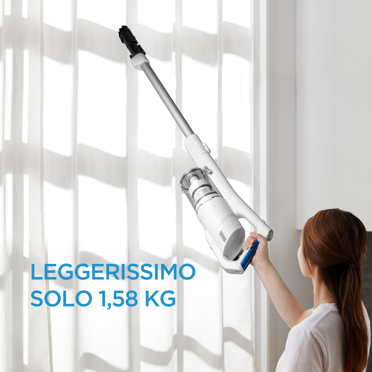 Una donna sostiene un aspirapolvere senza fili bianco e leggero vicino a una finestra luminosa.