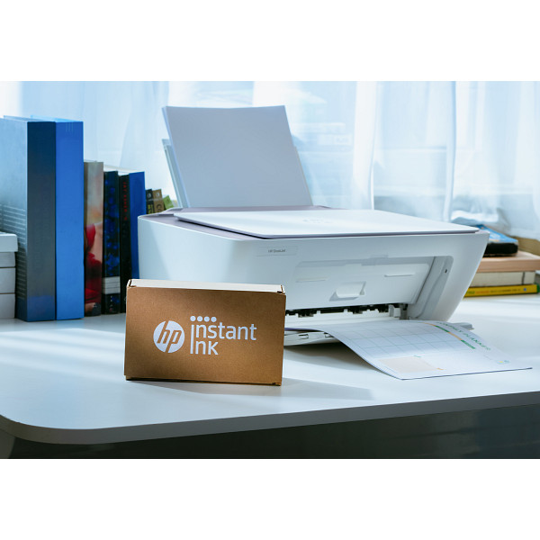 Ein weißer HP-Drucker steht auf einem Schreibtisch mit Büchern und einer HP Instant Ink-Box davor.