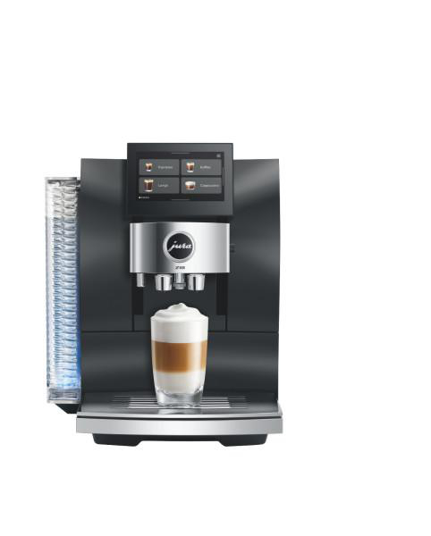 Eine schwarze Jura Kaffeemaschine mit Display und einer Glastasse Latte Macchiato auf der Abtropffläche.