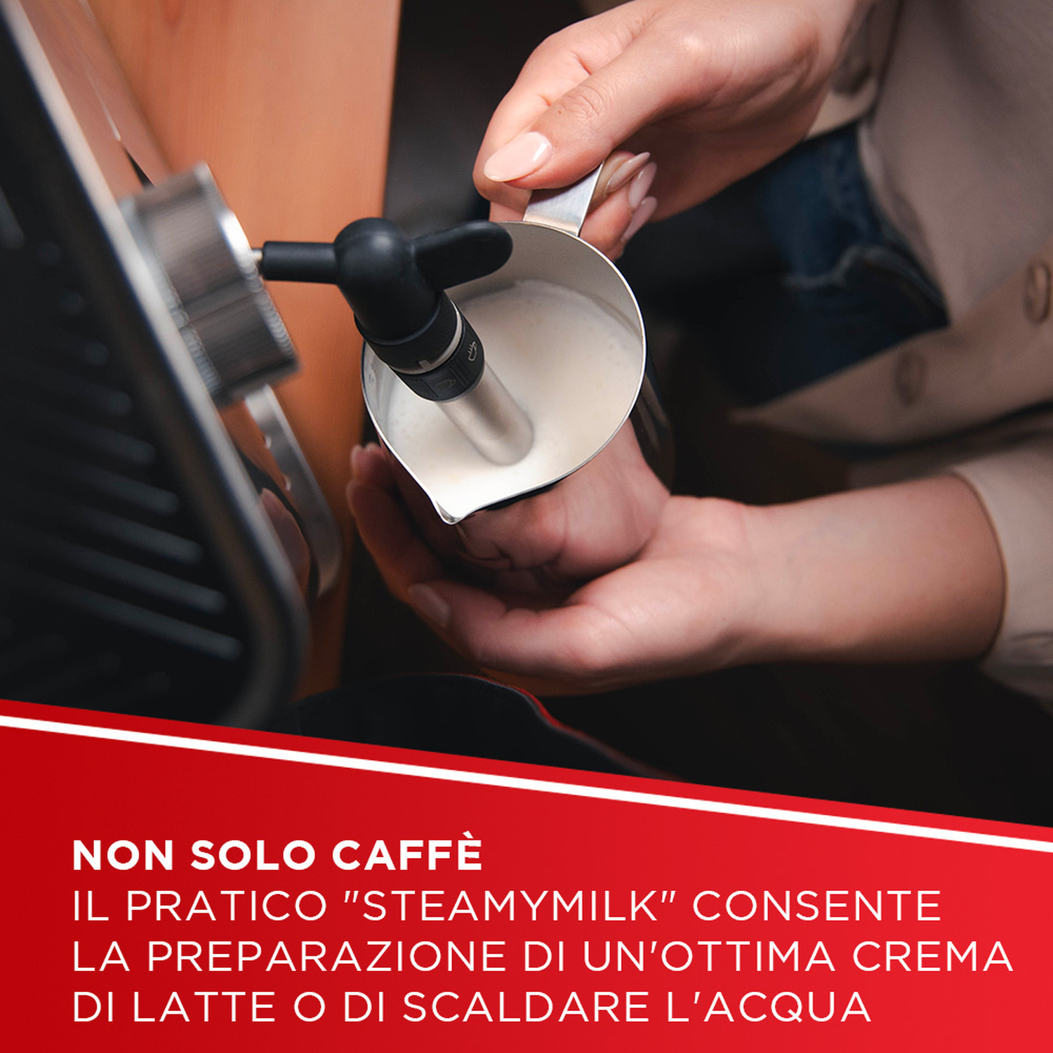 Una mano regge una lattiera mentre la macchina da caffè monta il latte.