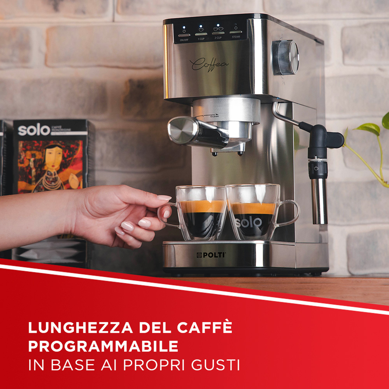 Una mano posiziona una tazzina di caffè davanti a una moderna macchina da caffè in acciaio inox con due tazze.