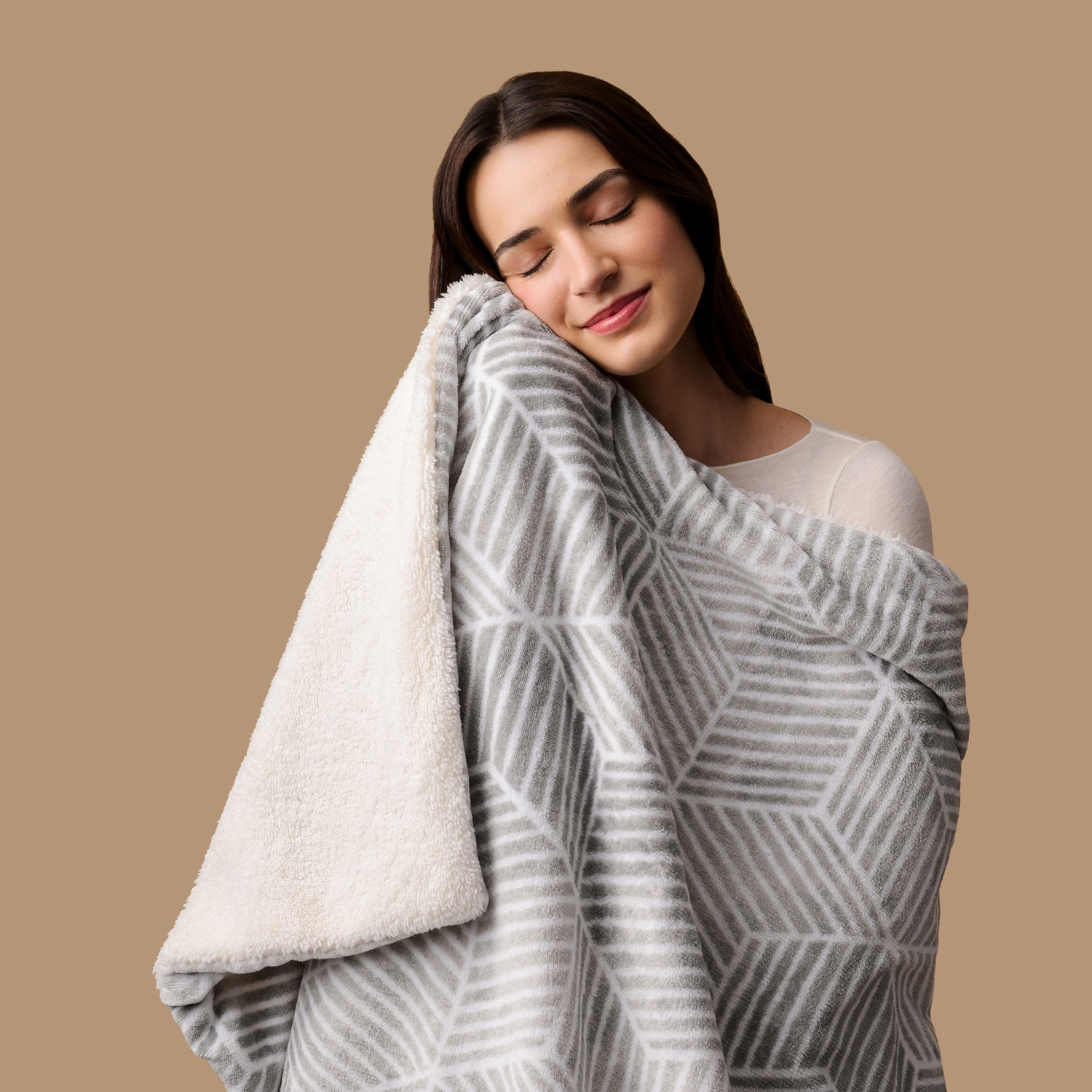 Una giovane donna preme felicemente il viso contro una morbida coperta con motivi grigi e bianchi.