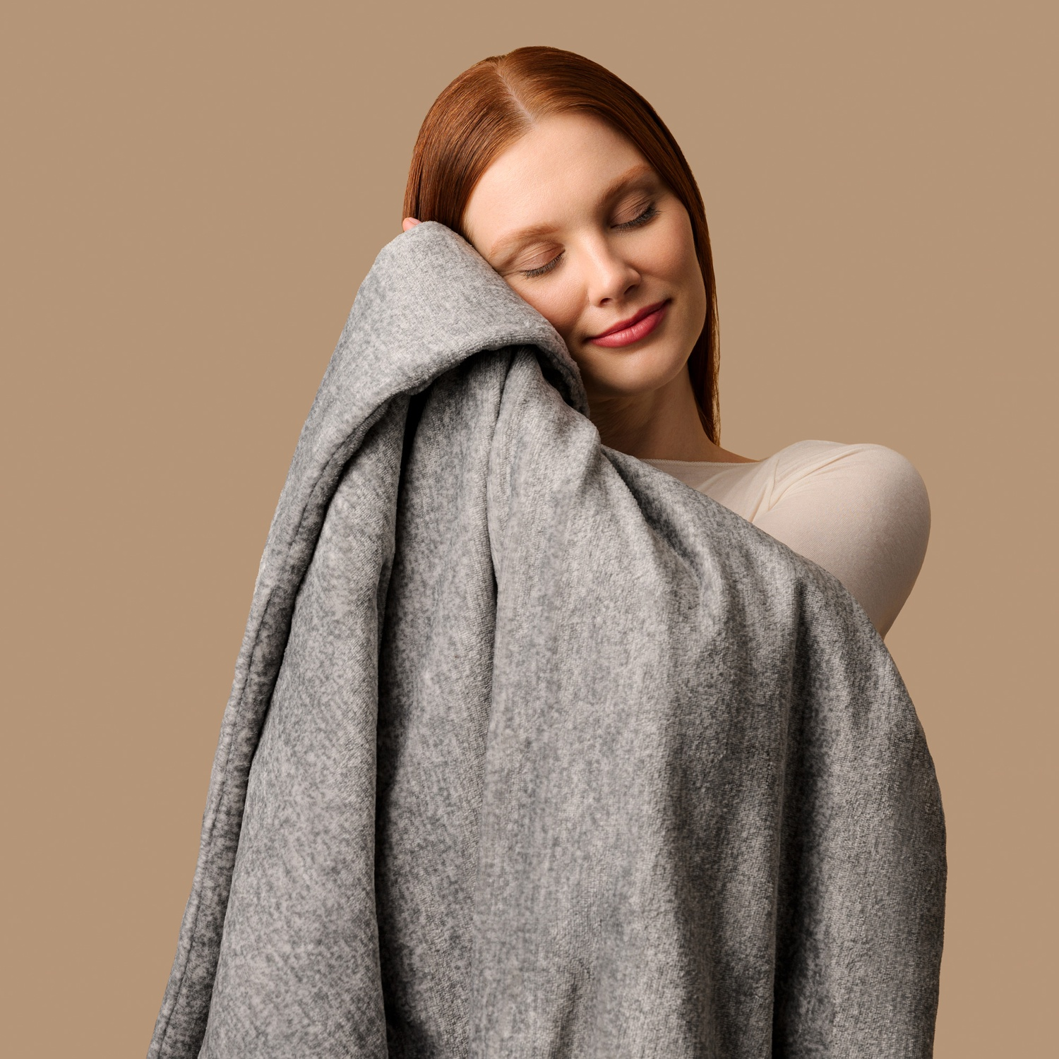 Una donna dai capelli rossi appoggia il viso su una morbida coperta grigia.