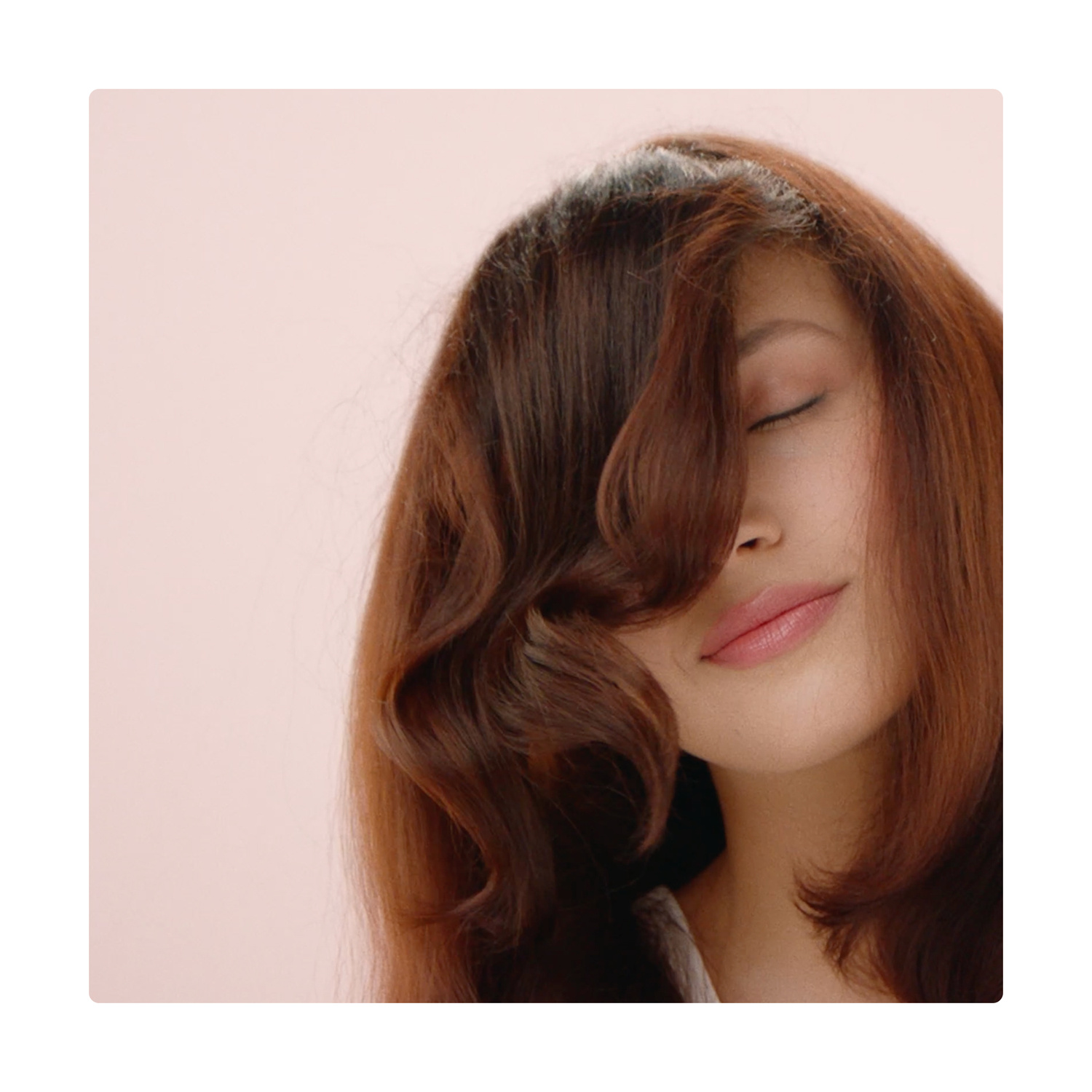 Una donna con gli occhi chiusi e capelli castano-rossicci che coprono un occhio, su sfondo rosa.