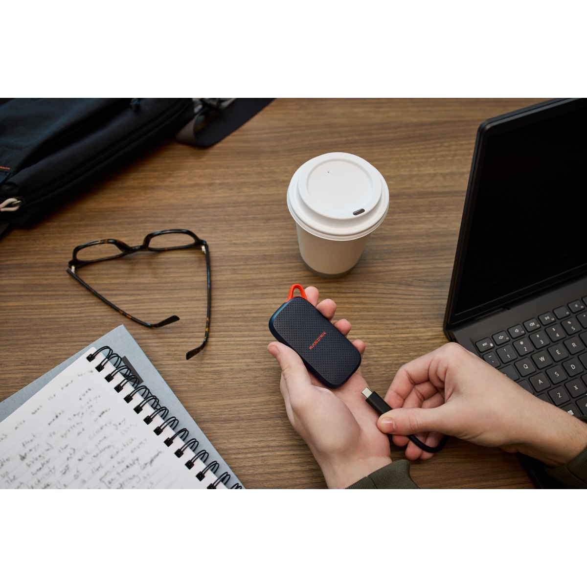 Una persona conecta una unidad portátil SanDisk mediante USB-C a una computadora portátil en un escritorio de madera.