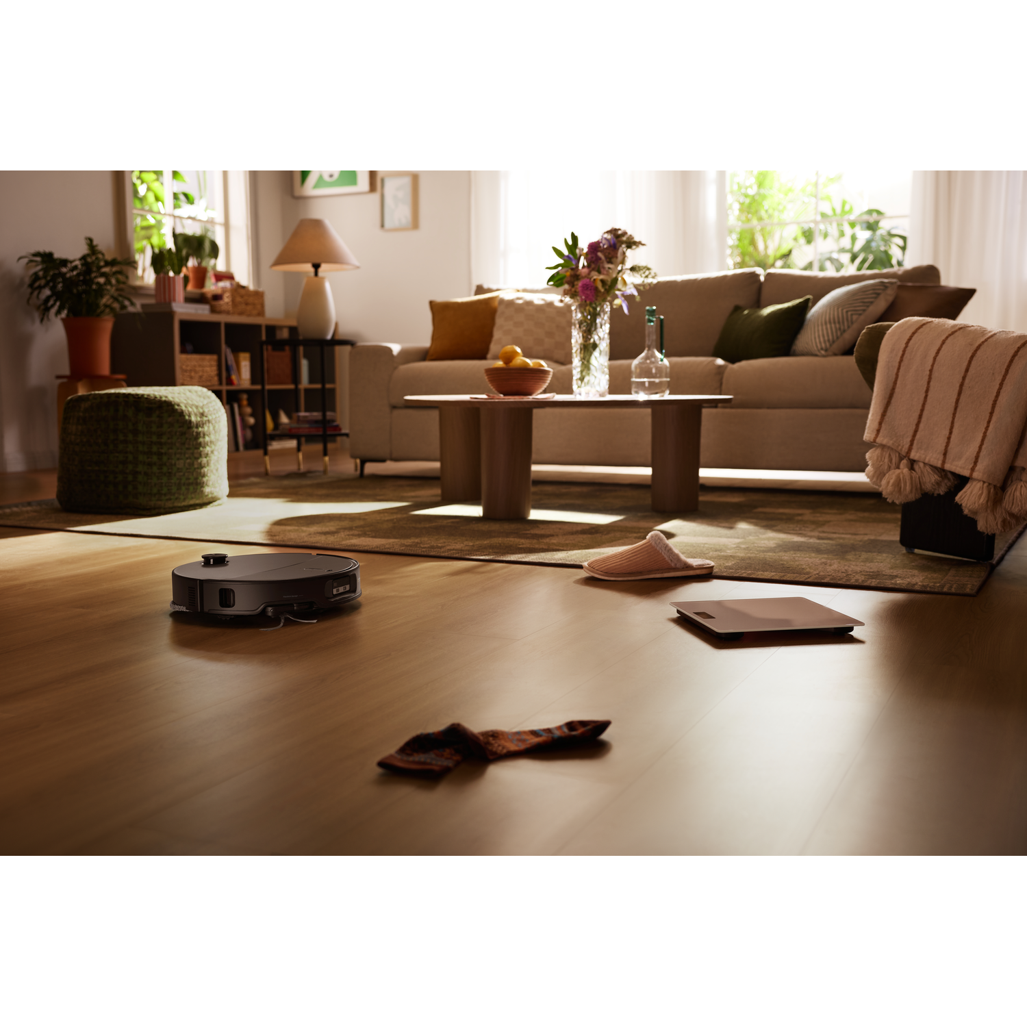 Un robot aspirateur sur un sol en bois dans un salon ensoleillé avec canapé et tapis.