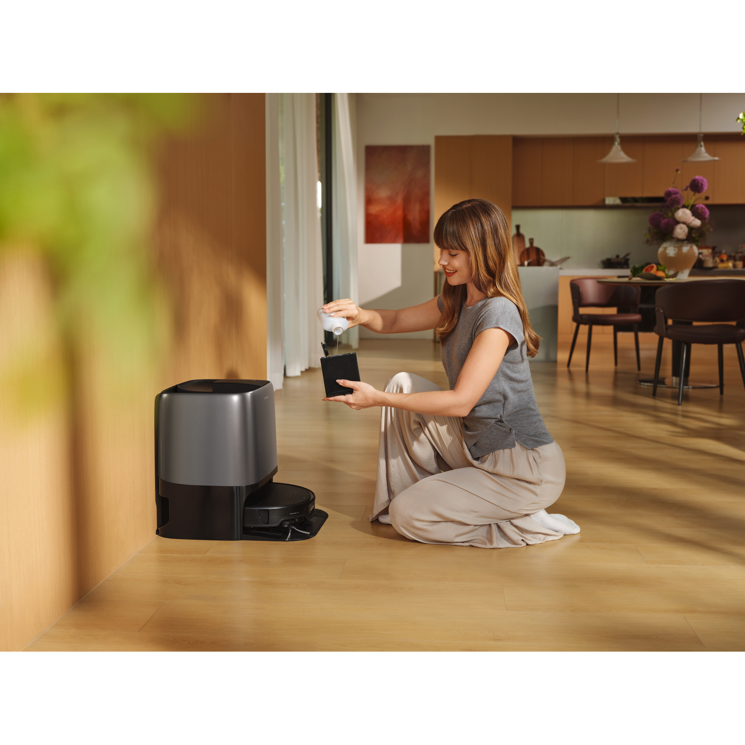 Une femme agenouillée sur un parquet remplit un petit récipient de liquide près d'une station d'aspirateur.