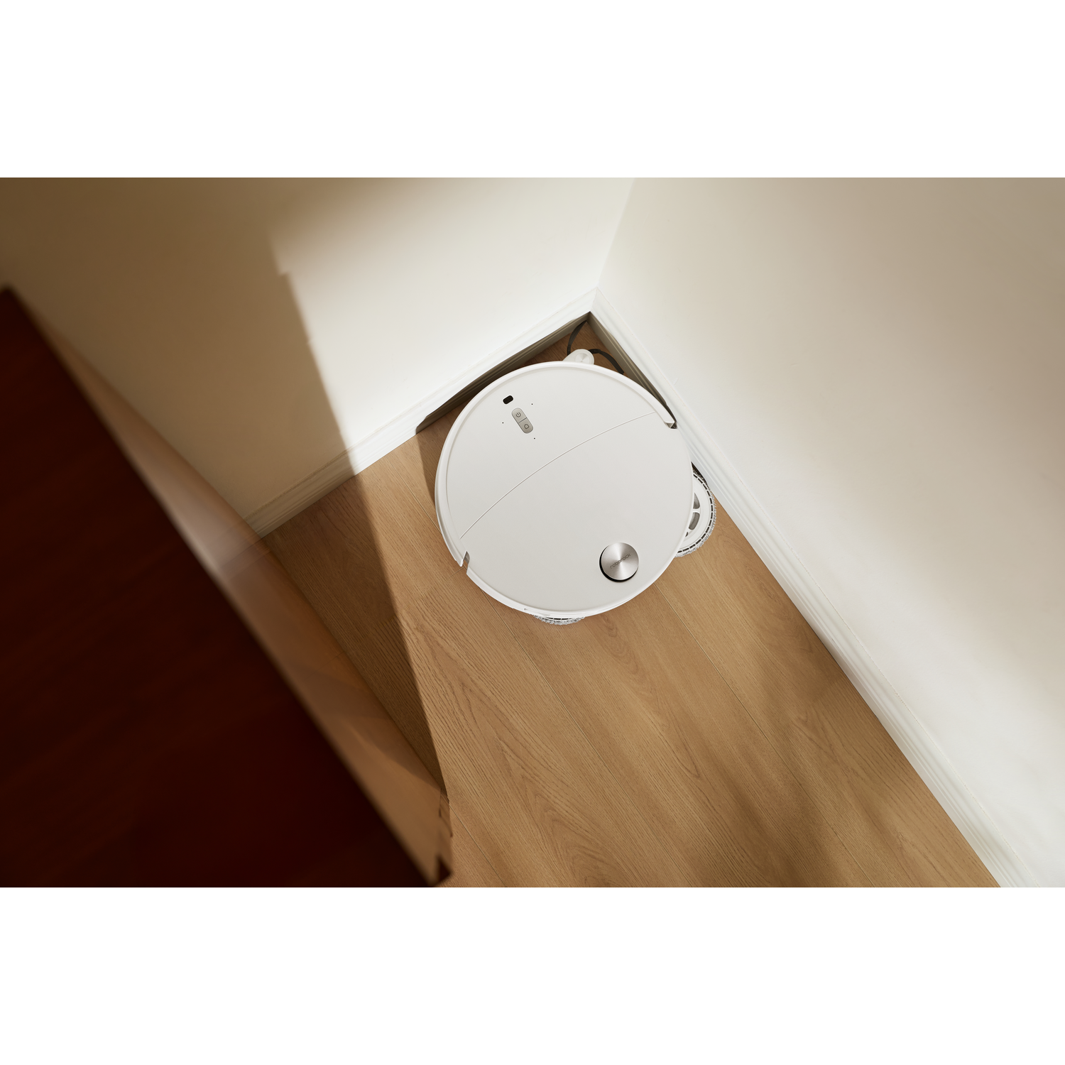 Un robot aspirateur blanc est placé dans le coin d'une pièce sur un sol en bois.