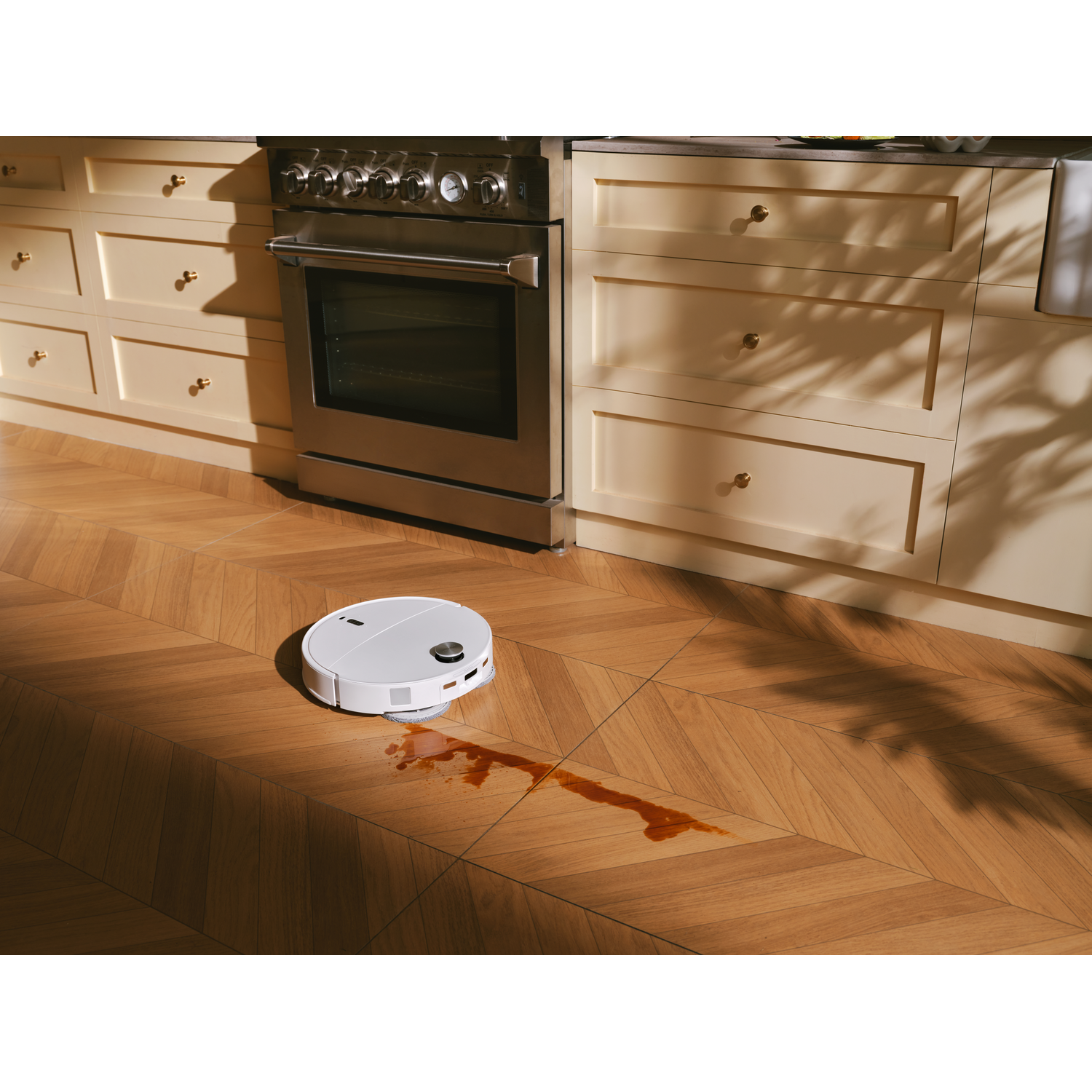 Un robot aspirateur blanc nettoie une tache de café sur un sol en bois dans une cuisine.