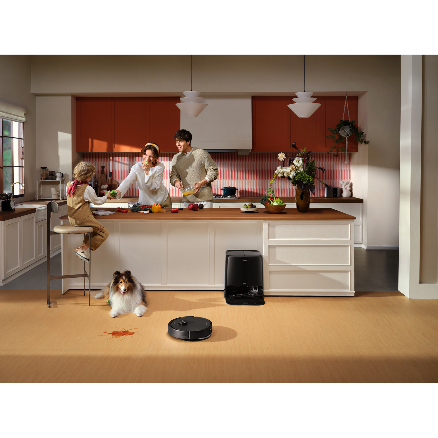Une famille cuisine dans une cuisine moderne avec un robot aspirateur et un chien sur le sol.