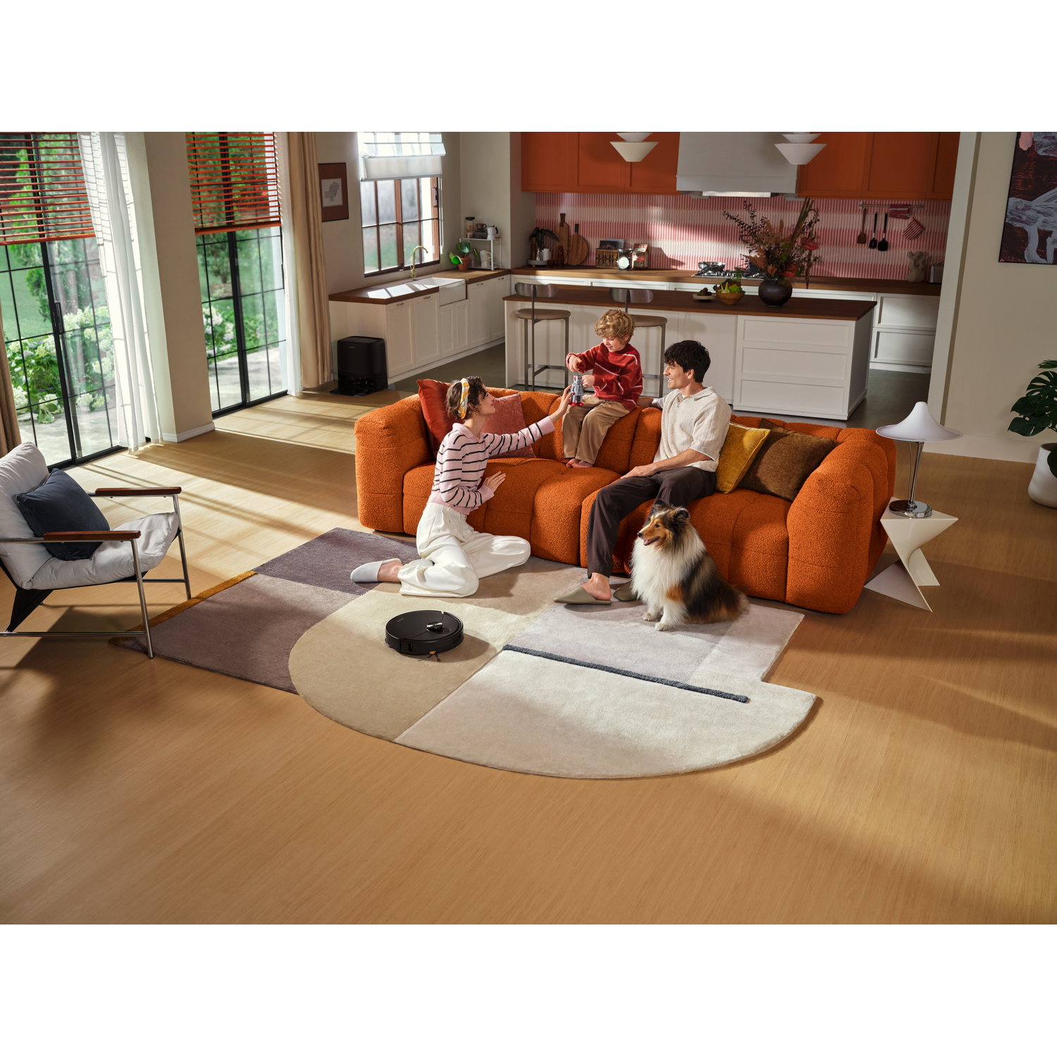 Une famille avec un enfant et un chien est assise sur un canapé orange dans un salon avec un robot aspirateur.