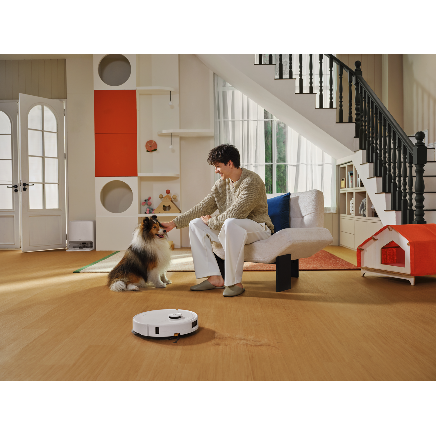 Un homme caresse un chien dans un salon pendant qu'un robot aspirateur se déplace sur le sol.