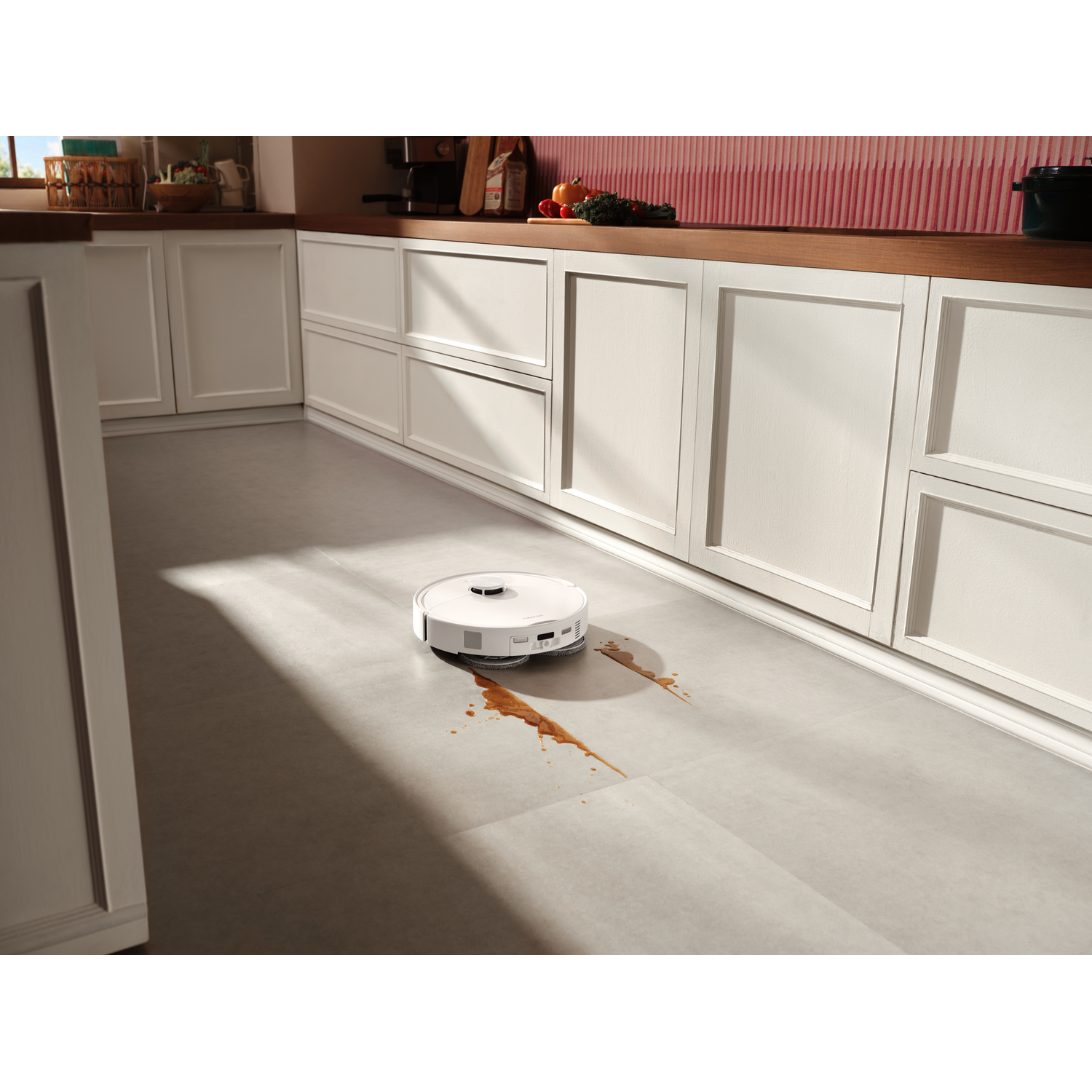 Un robot aspirateur blanc nettoie un liquide renversé sur un sol de cuisine moderne.