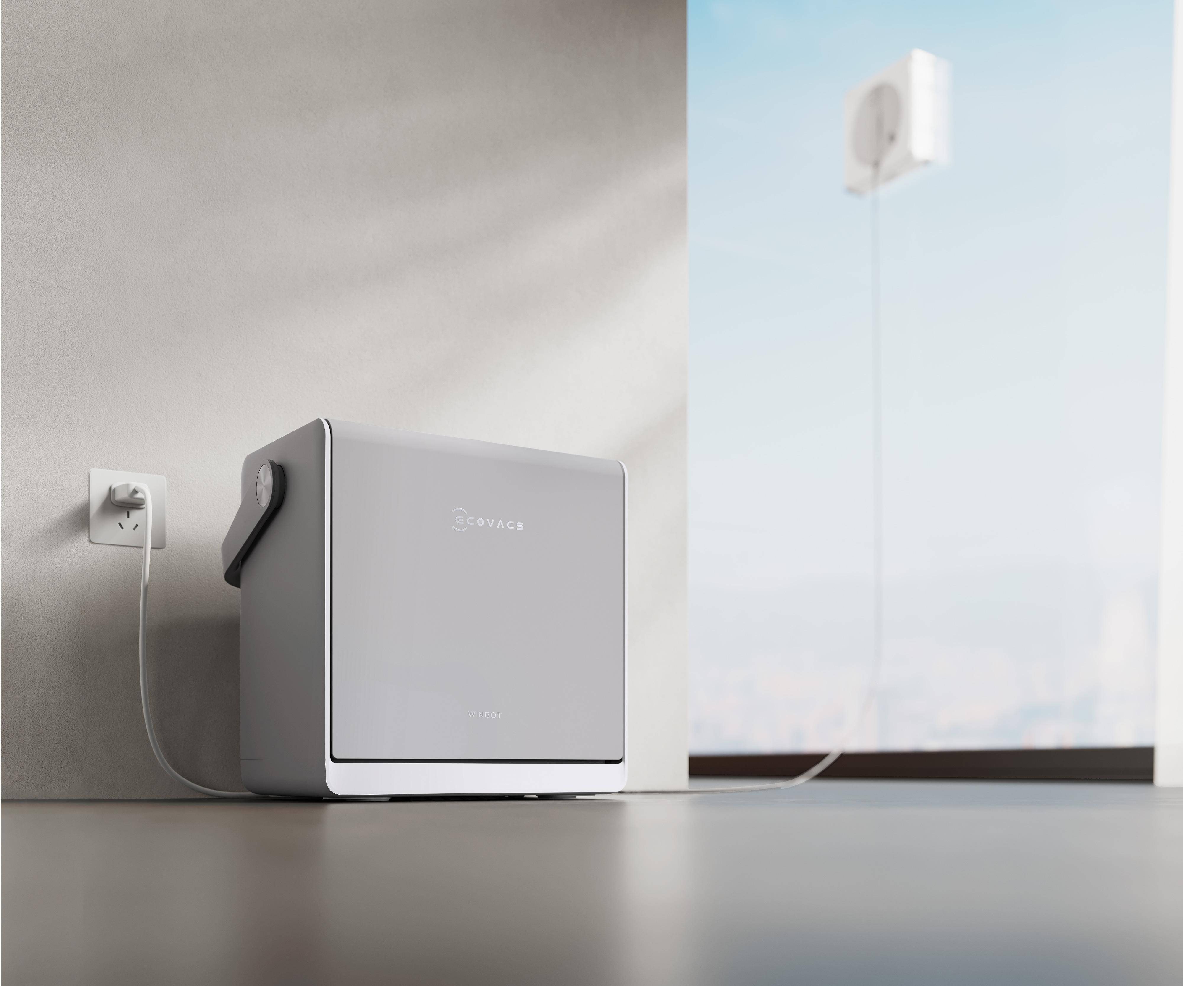 Eine weiße Ecovacs Winbot Ladestation steht auf dem Boden, verbunden mit einer Steckdose und einem Fensterputzroboter.
