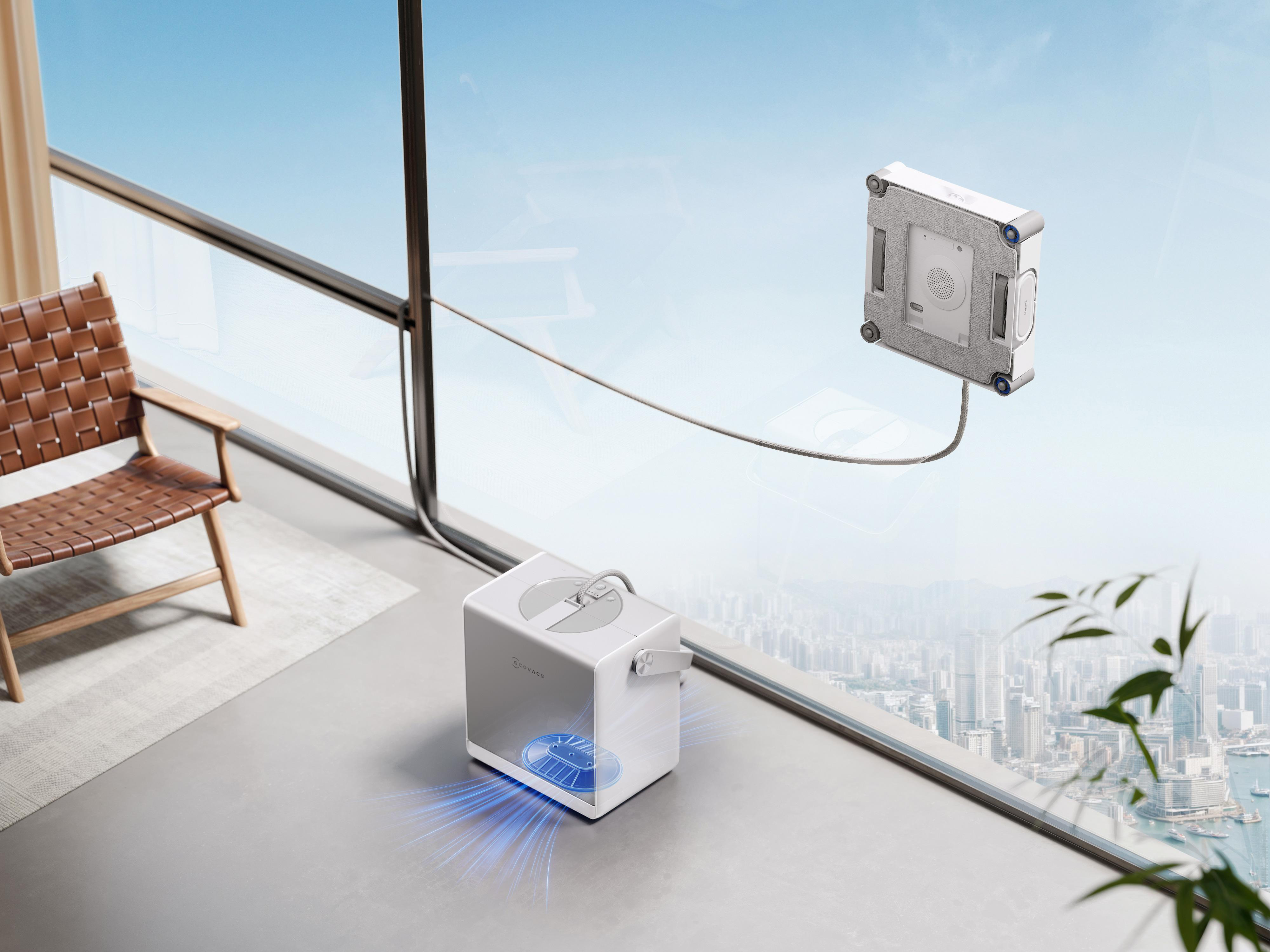 Ein weißer Fensterputzroboter haftet an einer Hochhaus-Glasscheibe und ist mit einer Basisstation verbunden.