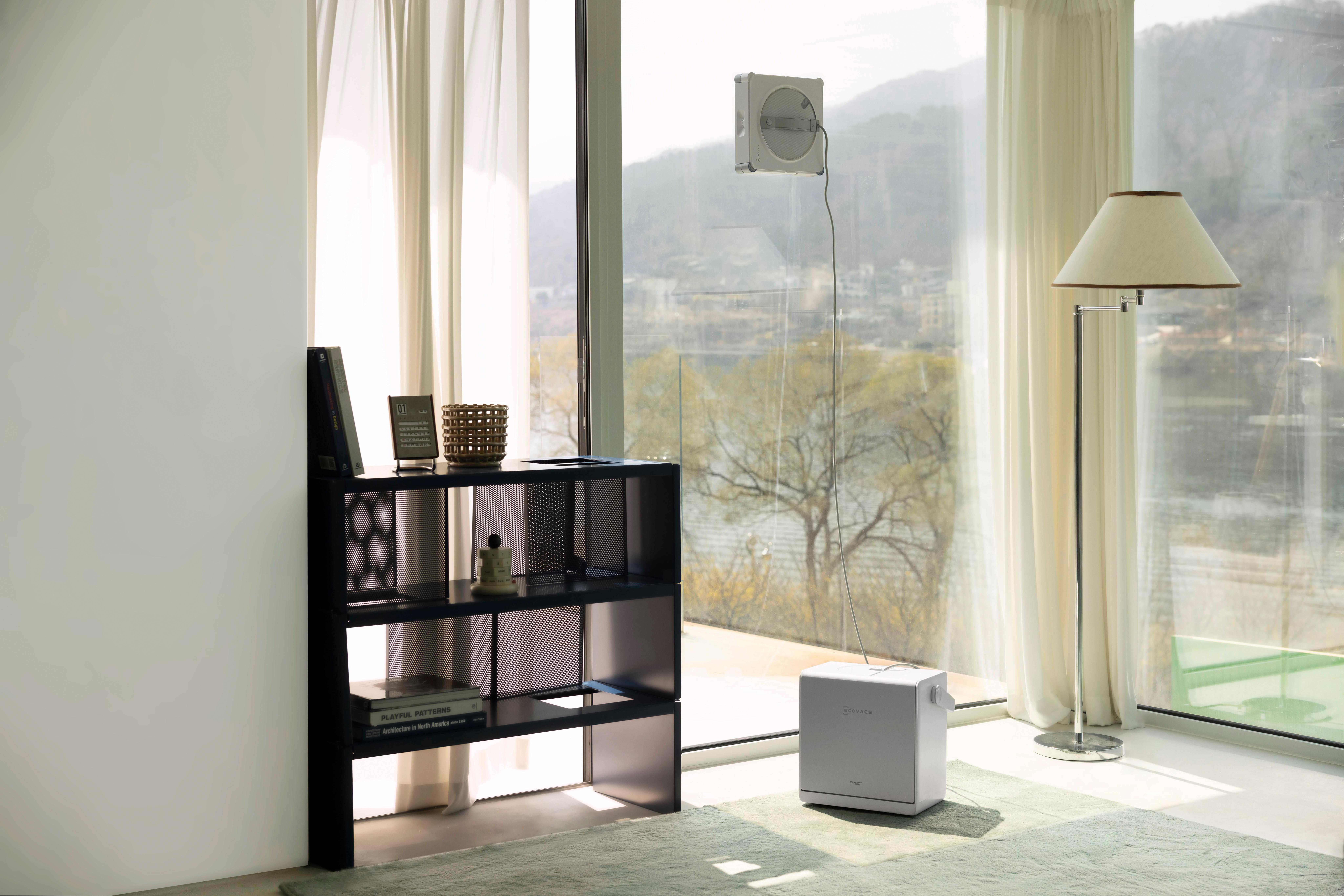 Ein automatischer Fensterputzer reinigt eine große Fensterscheibe in einem hellen, modernen Wohnzimmer.