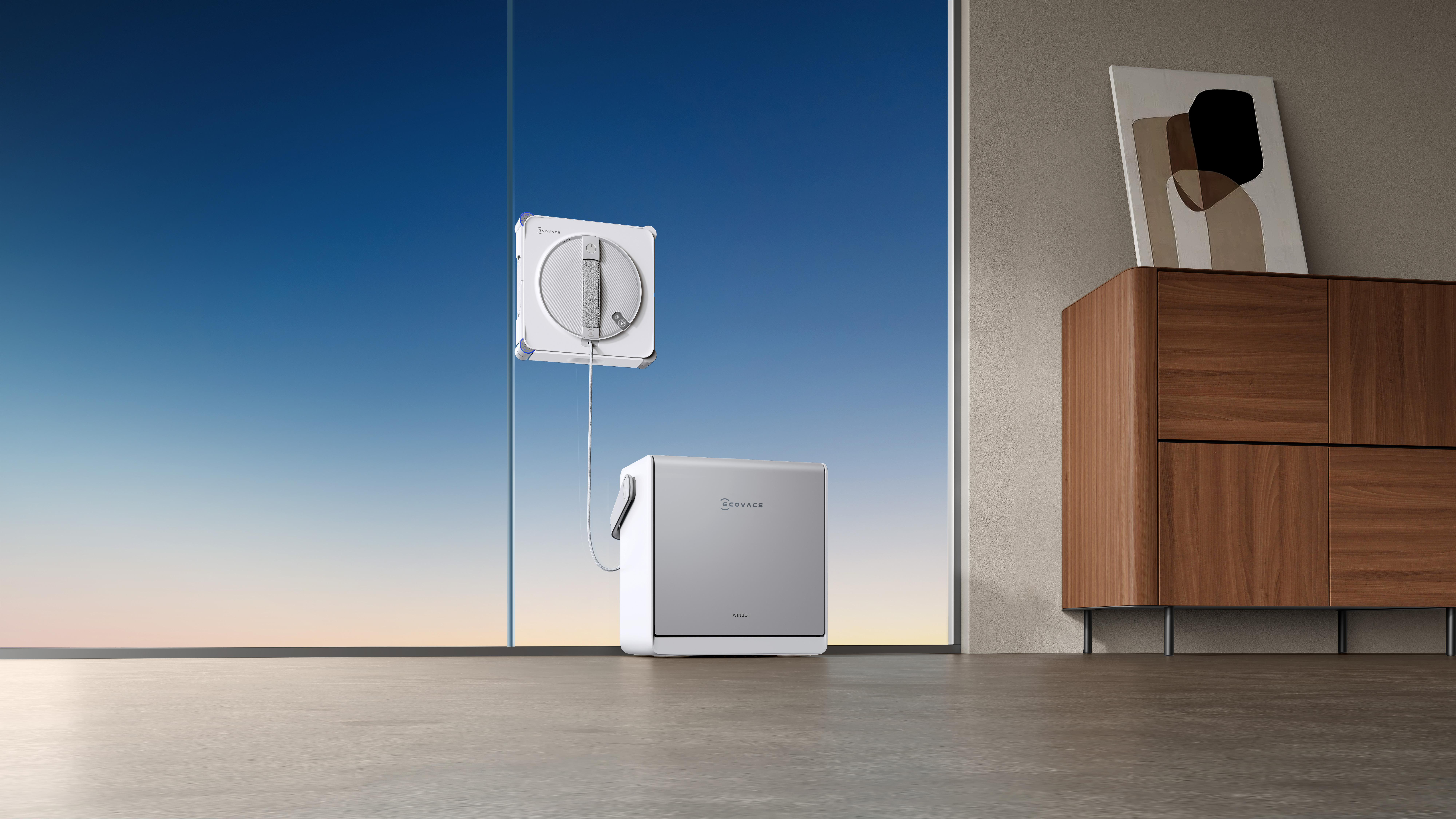 Ein weißer Ecovacs-Fensterreinigungsroboter reinigt eine Fensterscheibe vor einem blauen Himmel.