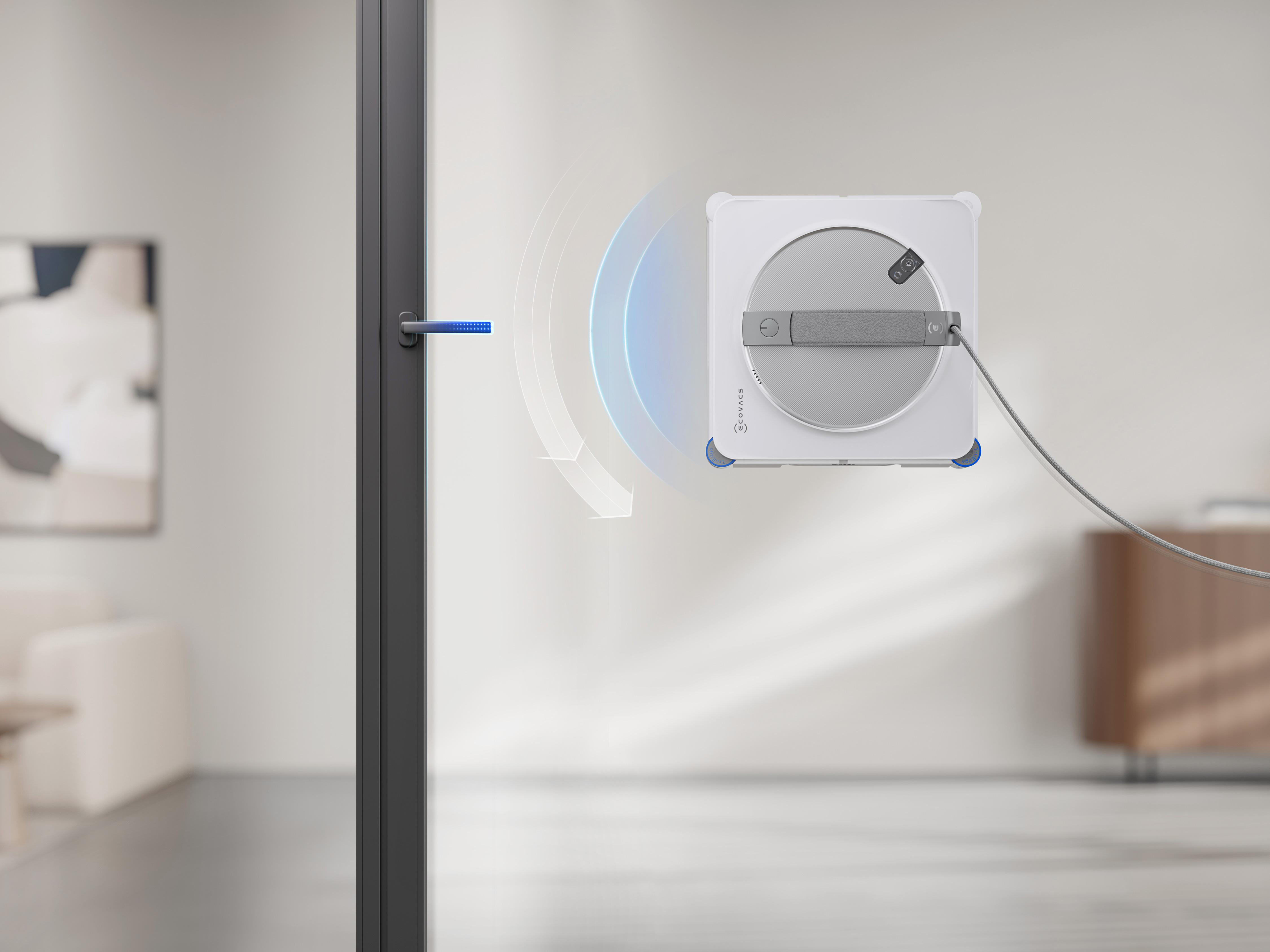 Ein weißer, quadratischer Fensterreinigungsroboter hängt an einer Glastür mit einem langen Stromkabel.
