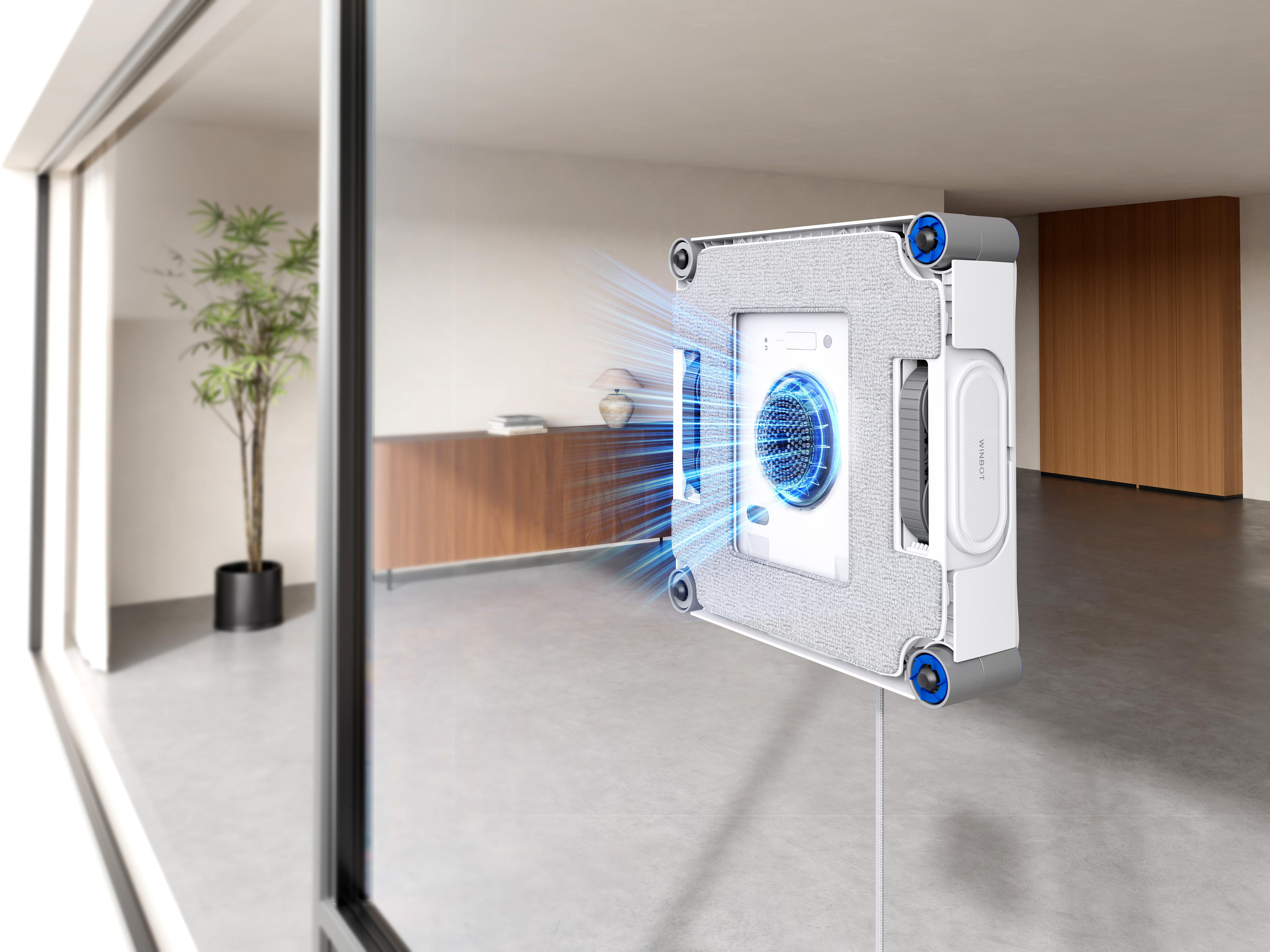 Ein weißer, quadratischer Fensterreinigungsroboter reinigt eine Glaswand mit blauem Sprühnebel.