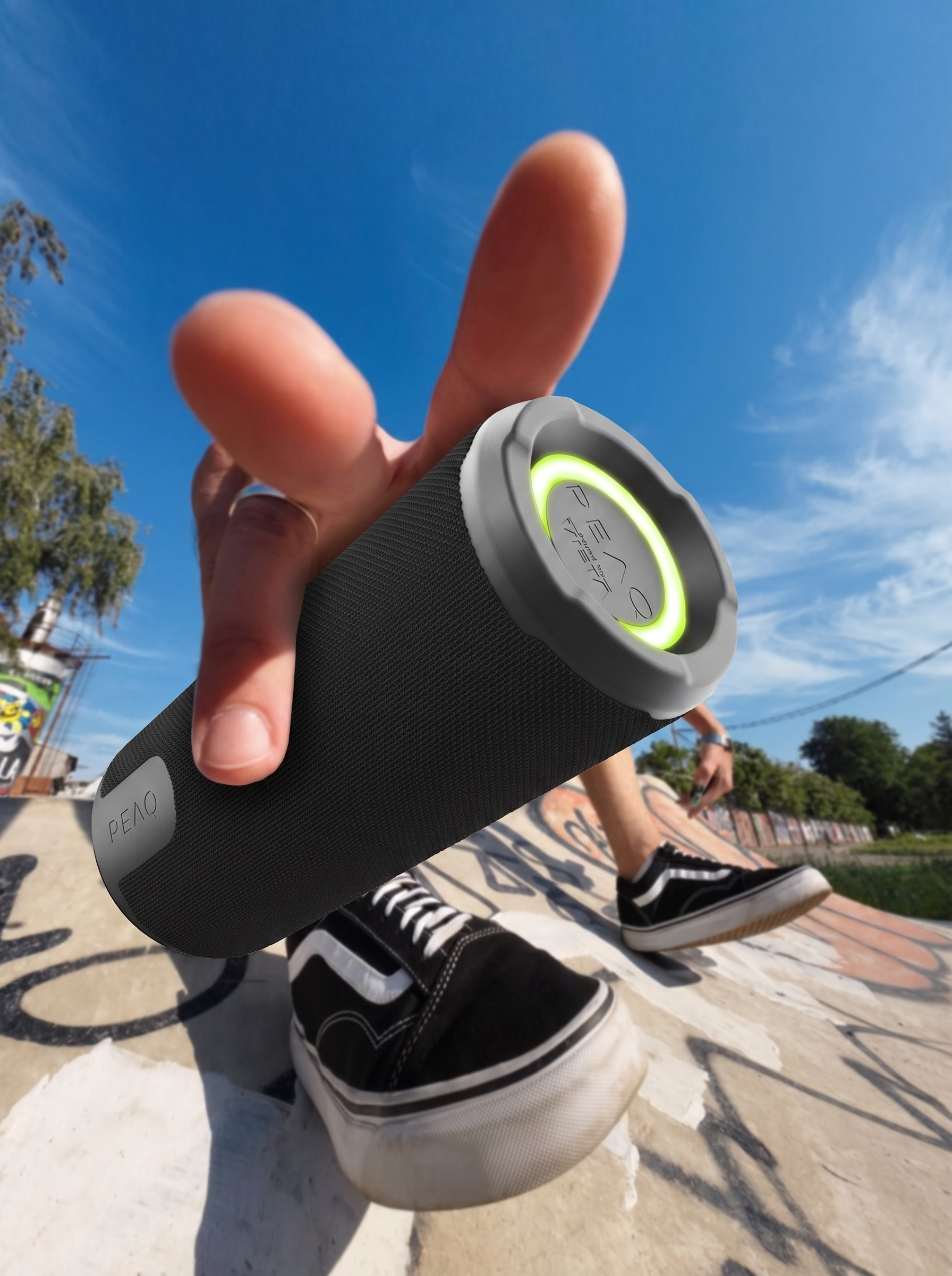 Una persona sostiene un altavoz Bluetooth negro frente a un skatepark.