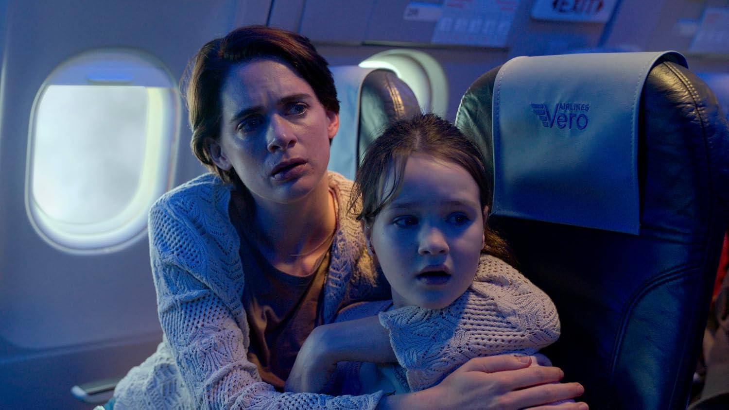 Eine besorgte Mutter hält ihre Tochter auf einem Flugzeugsitz in bläulichem Licht fest.