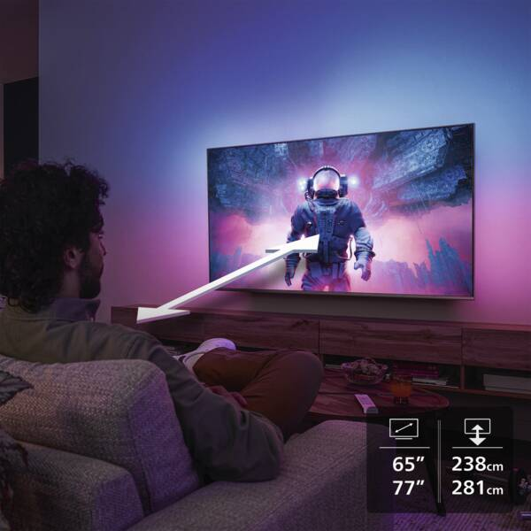 Ein Mann sitzt auf einem Sofa und schaut fern, während im Hintergrund violettes Licht an der Wand leuchtet.