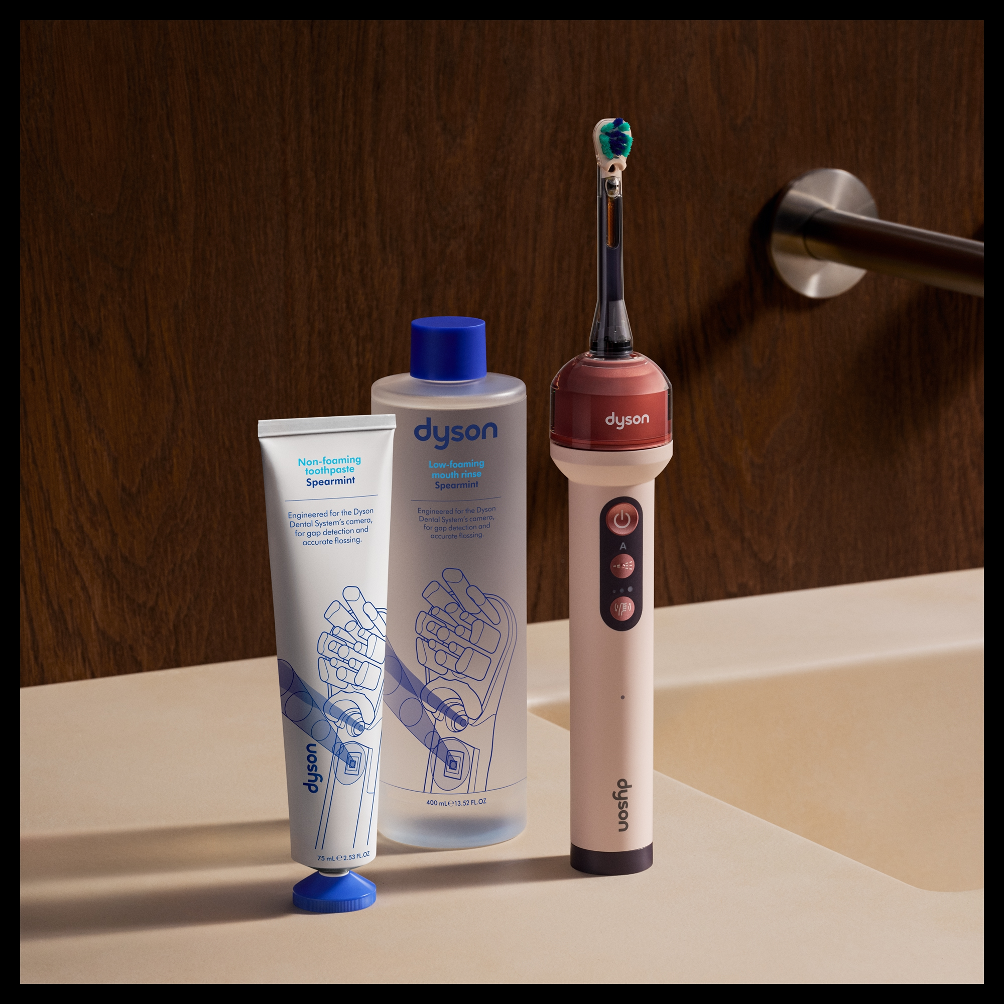 Une brosse à dents électrique Dyson, un bain de bouche et du dentifrice sur un comptoir de salle de bains en bois.