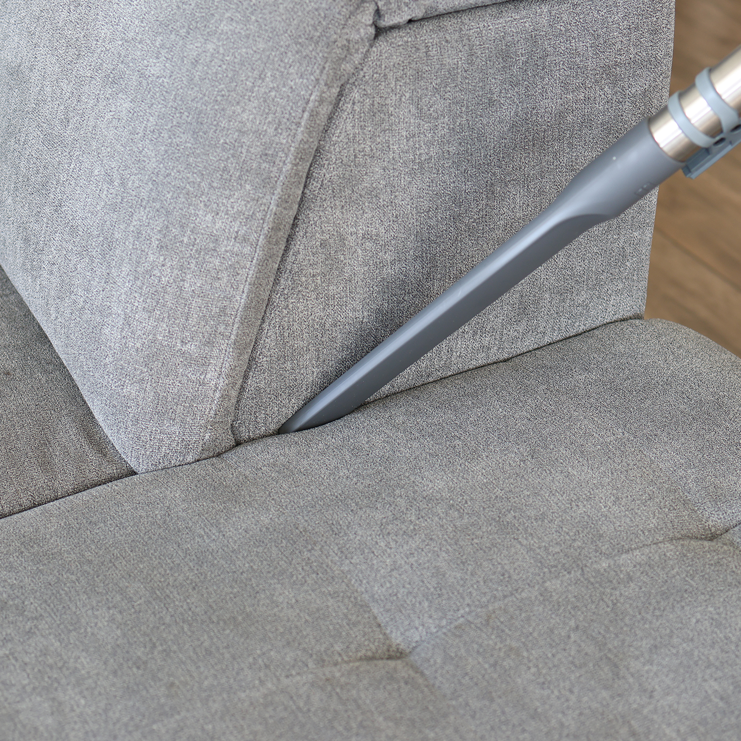 Ein Staubsaugeraufsatz reinigt die Ritzen eines grauen Sofas.