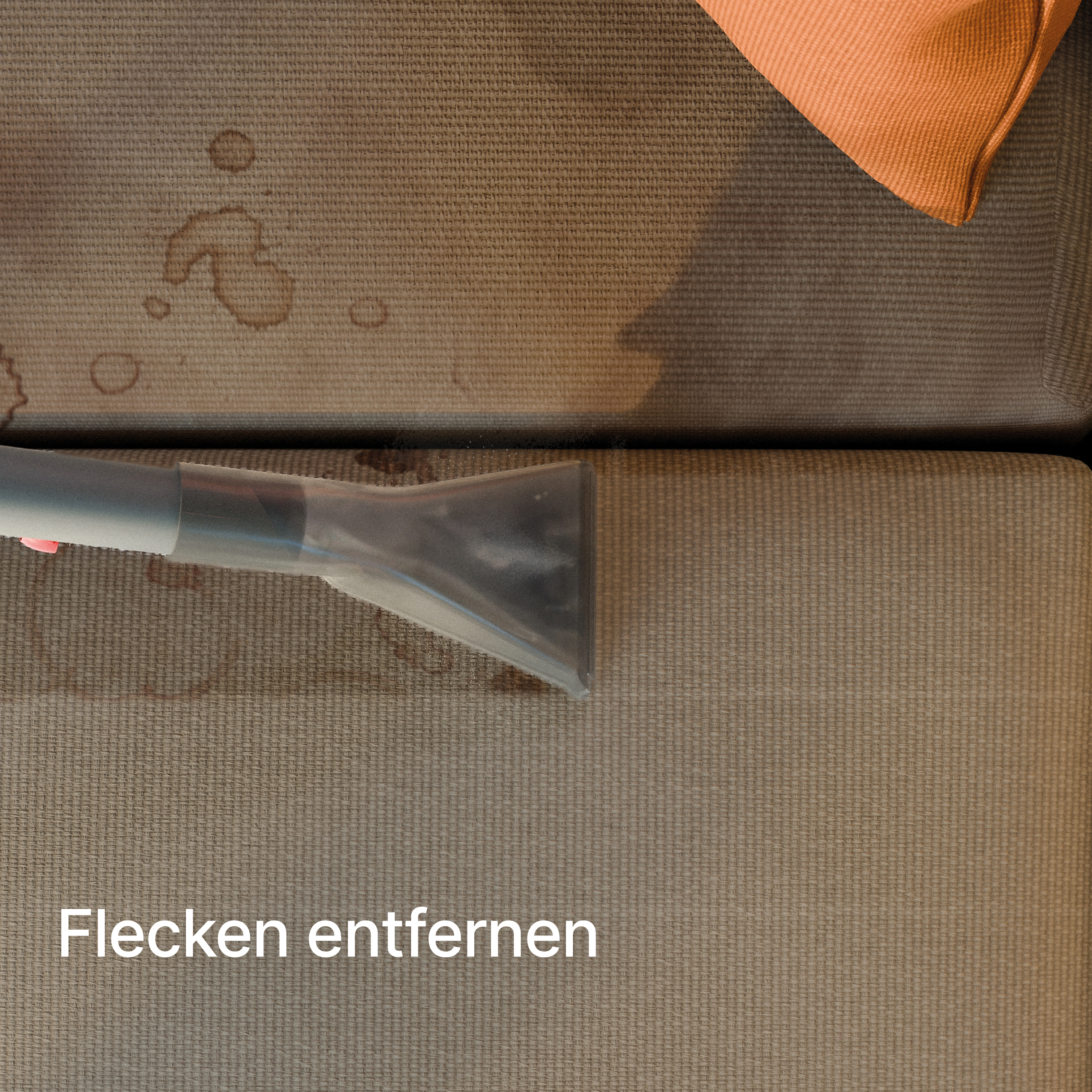 Ein Staubsaugeraufsatz entfernt Flecken von einem beigen Sofa, mit einem orangen Kissen.