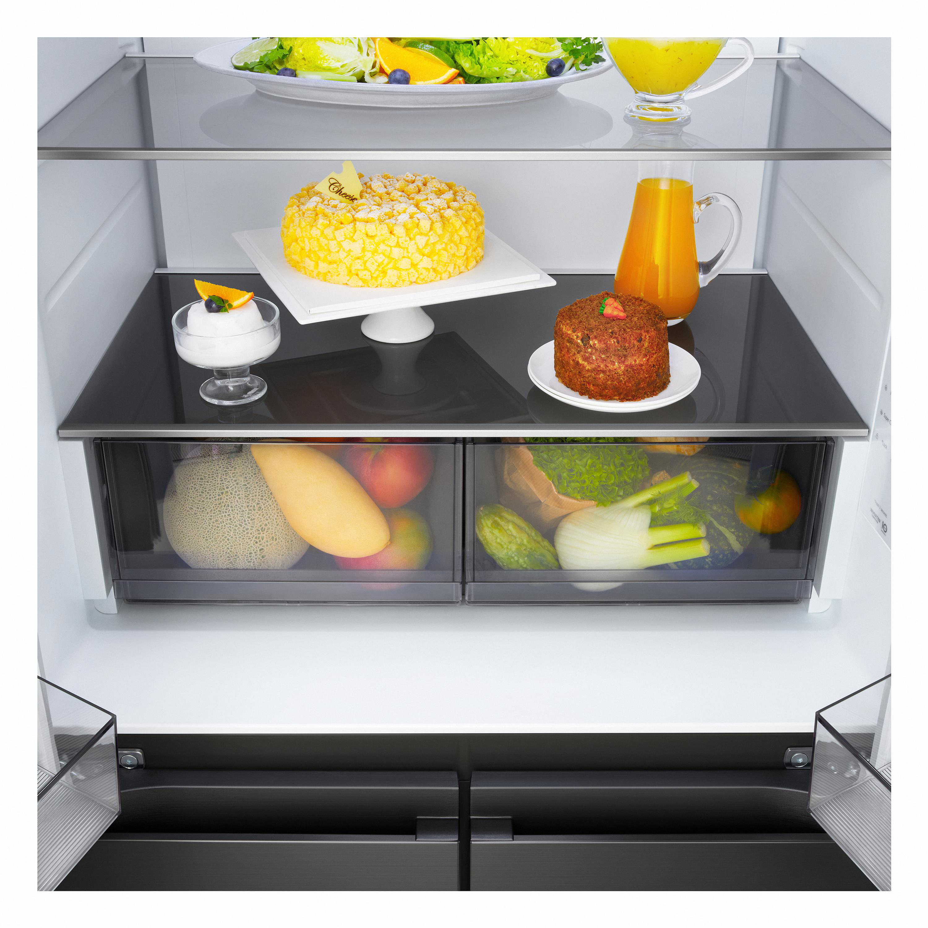 Ein sauberer Kühlschrank mit frischem Obst, Salat, einem Kuchen, Säften und Desserts auf den Glasböden und in den Fächern.