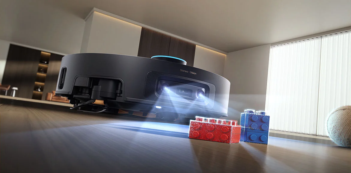 Egy fekete robotporszívó sztereó kamerákkal pásztázza a padlót, és vörös meg kék játékkockákat észlel.