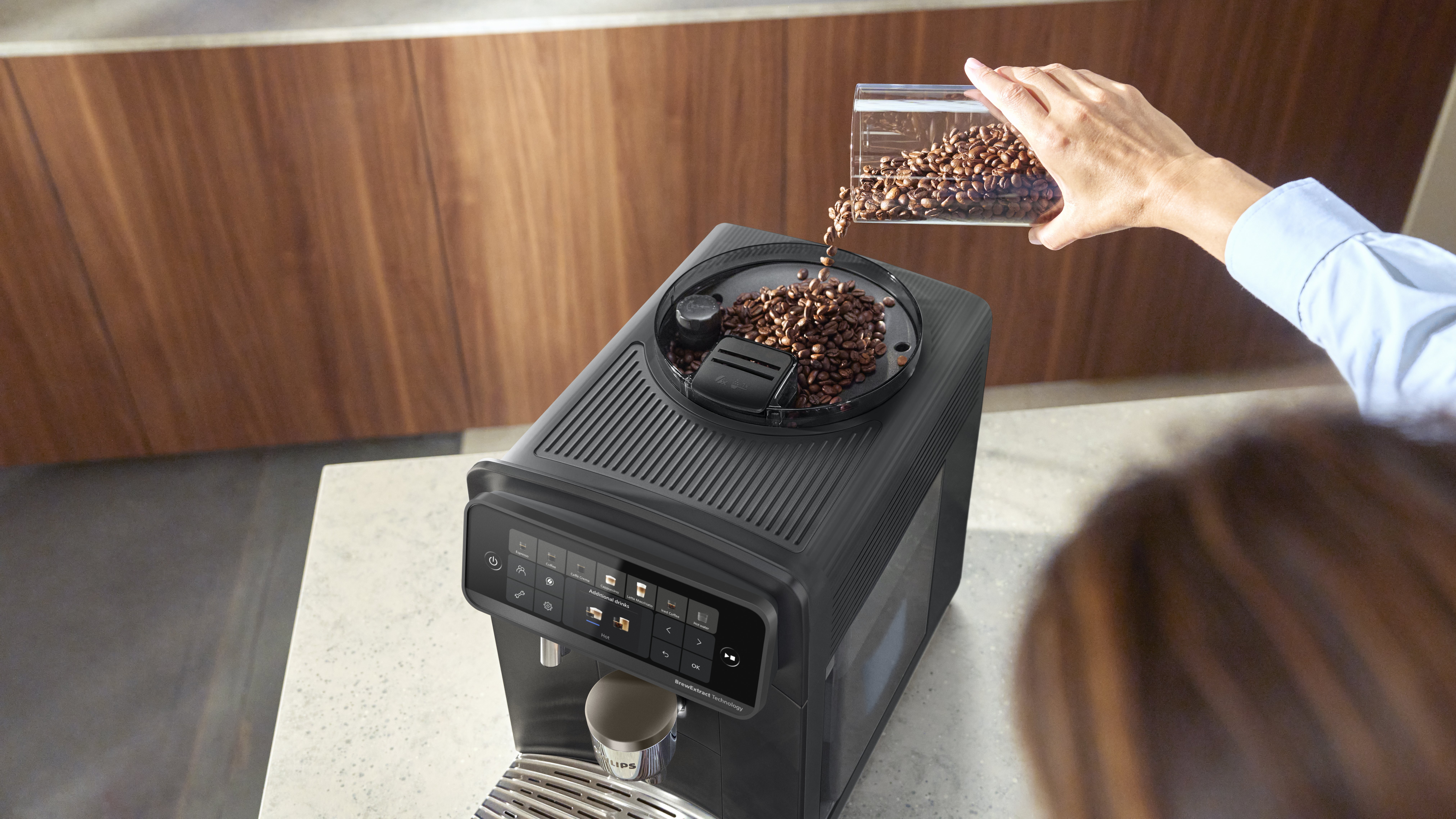 Eine Person gießt Kaffeebohnen in den Behälter einer modernen schwarzen Kaffeemaschine.