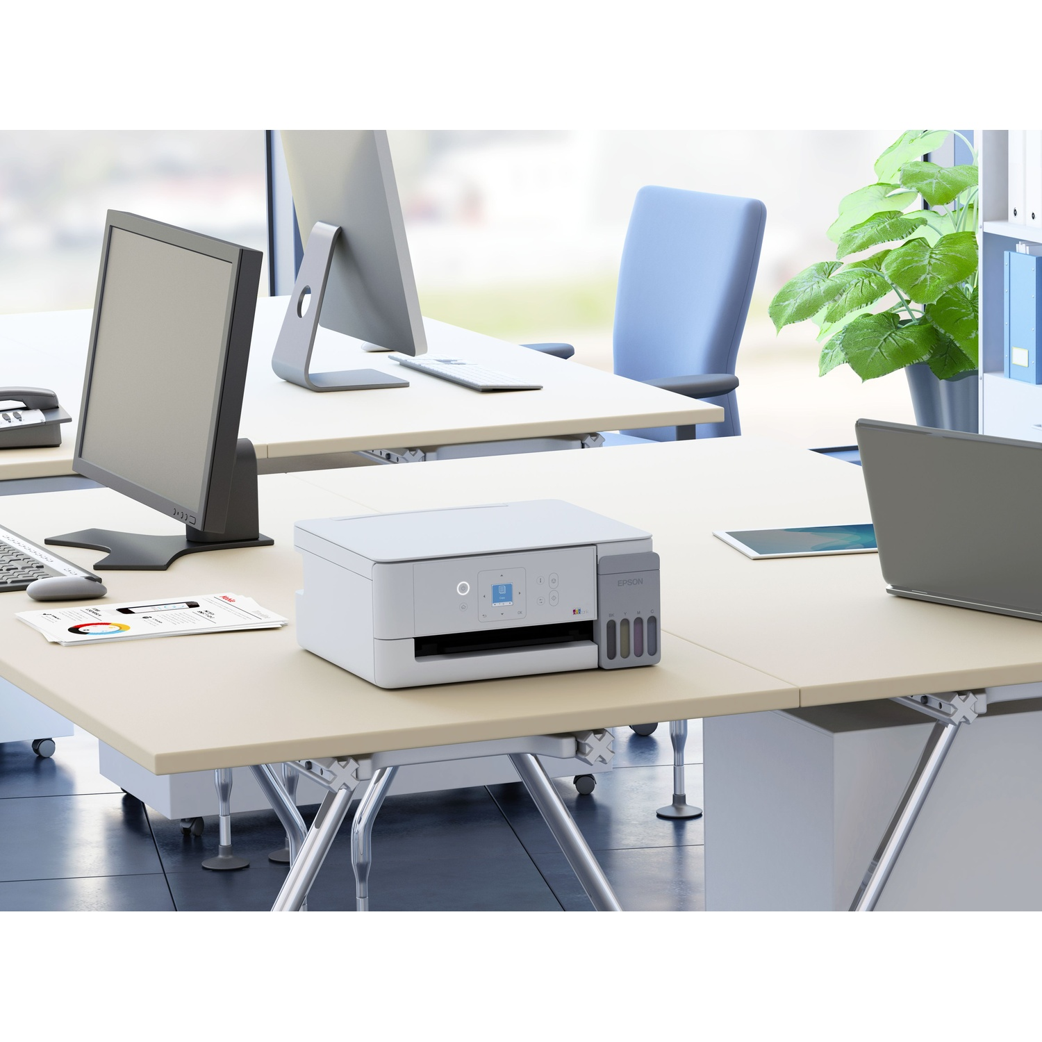 Una stampante Epson bianca è su una scrivania da ufficio chiara con computer e una pianta verde.