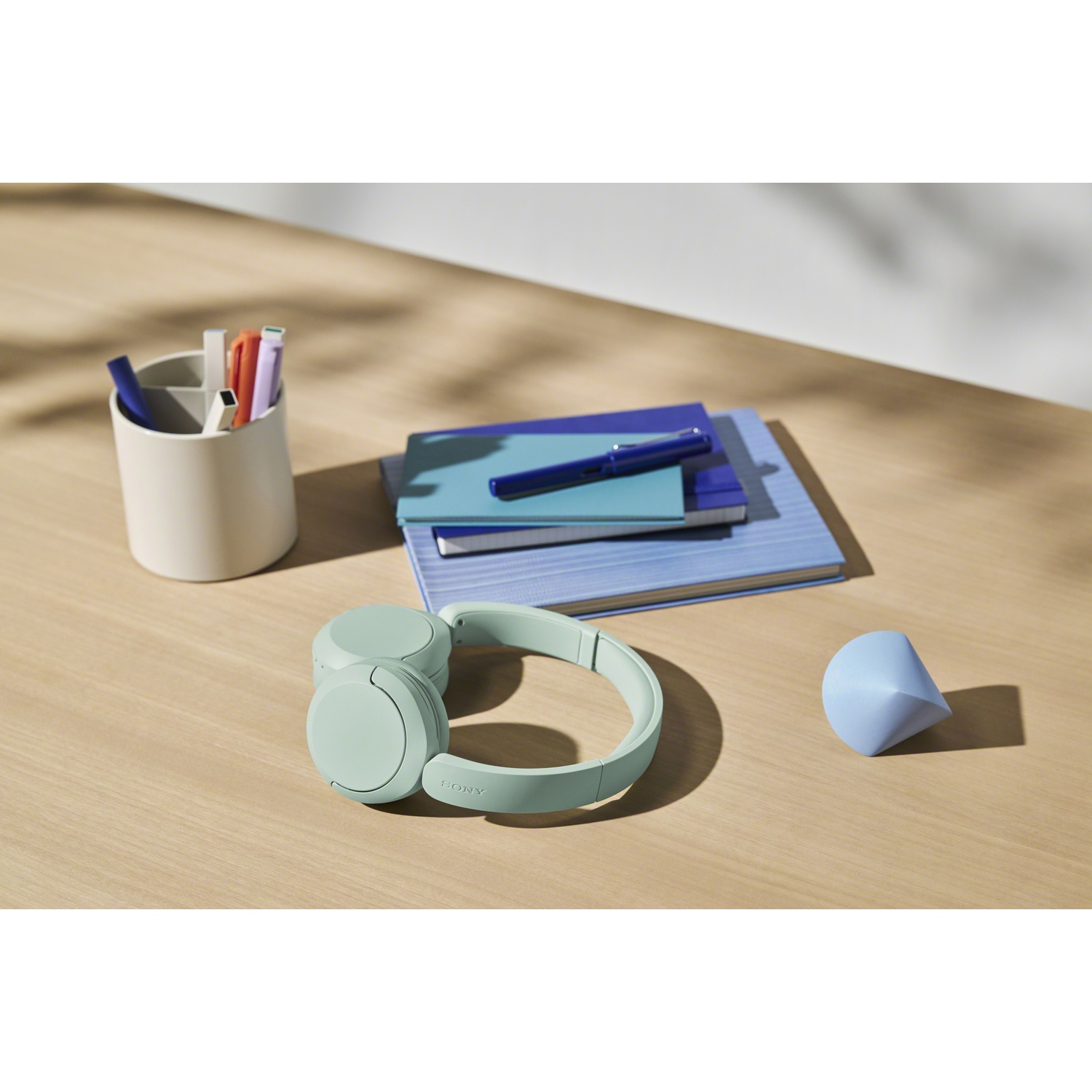 Des écouteurs verts reposent sur un bureau en bois avec des cahiers et un porte-stylos.