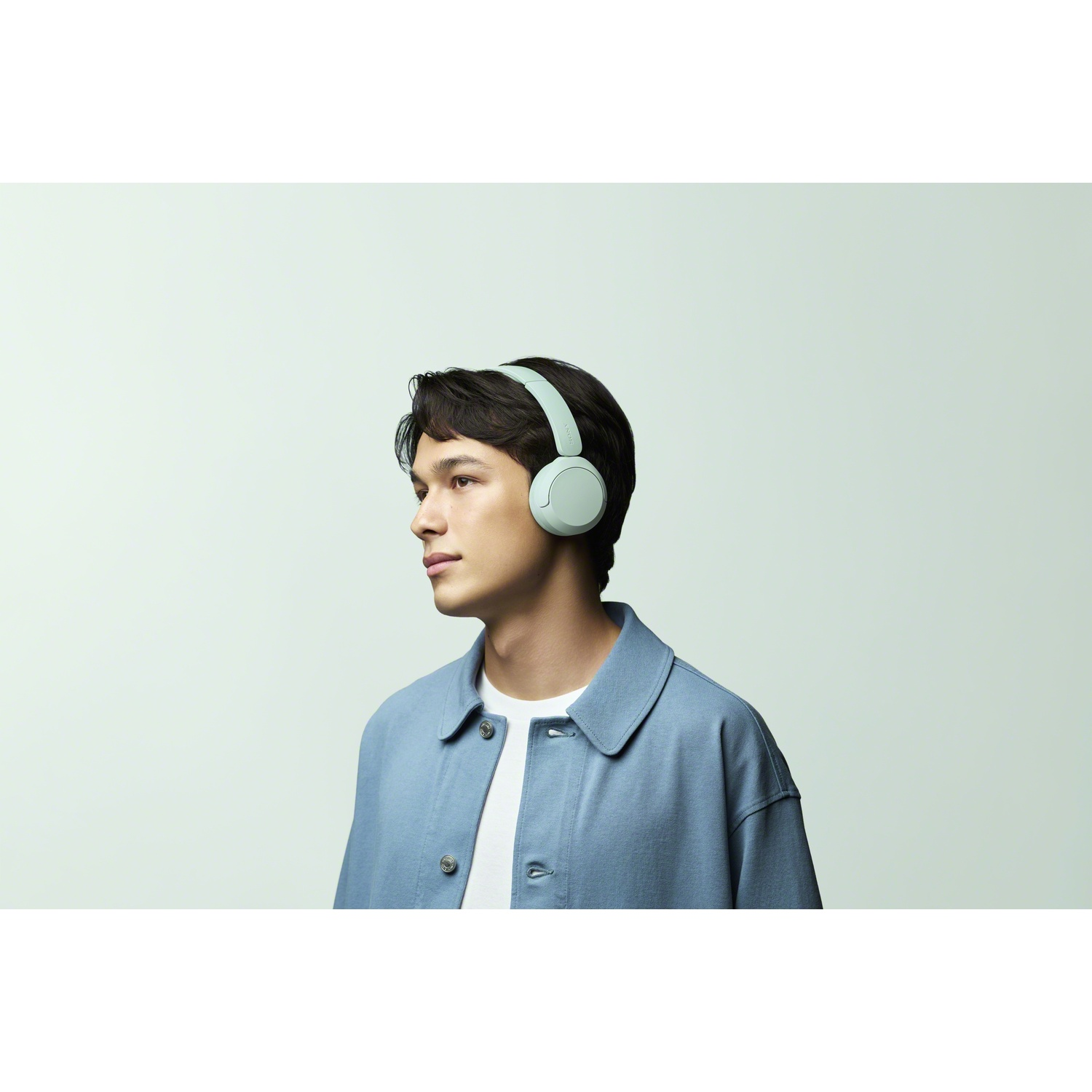 Un jeune homme aux cheveux sombres porte un casque vert menthe et une veste bleue sur fond clair.