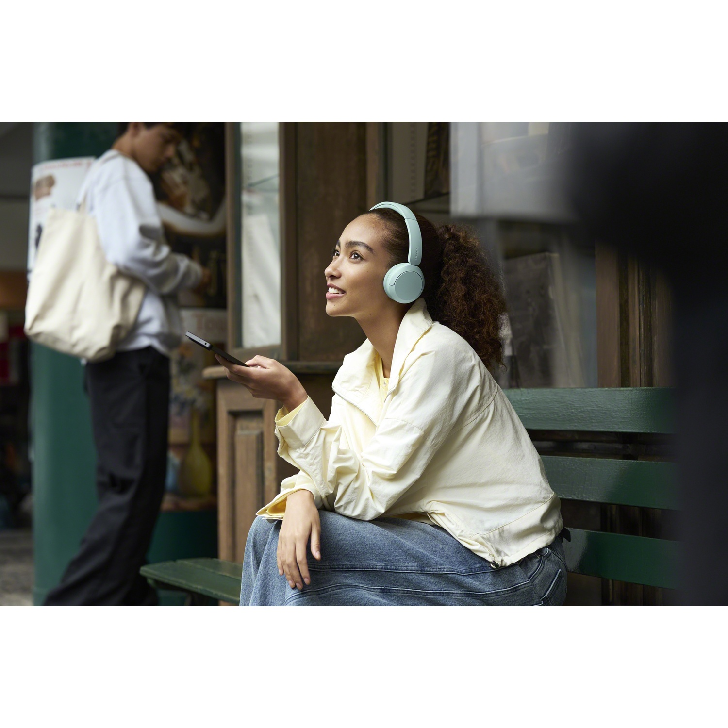 Une jeune femme avec un casque est assise sur un banc en tenant un smartphone.