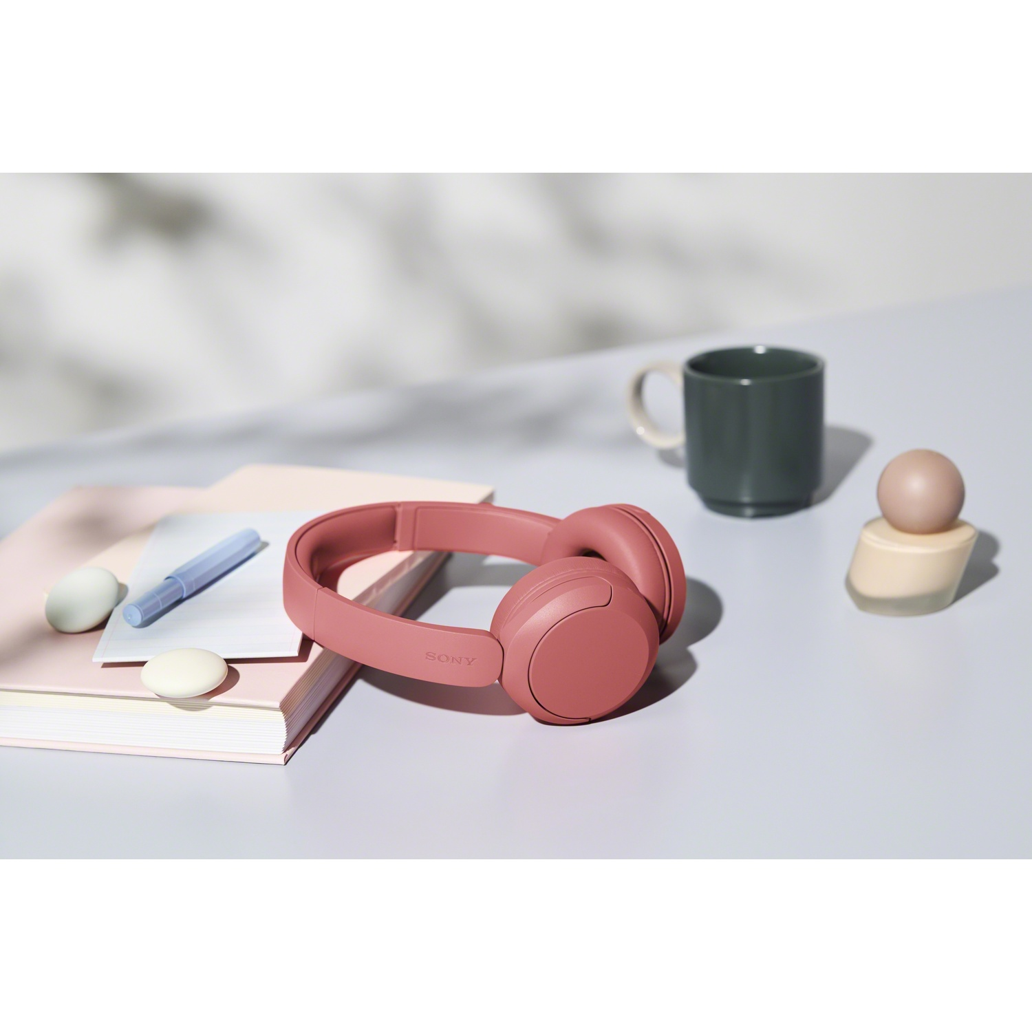 Casque rose sur une table à côté de carnets, d'un stylo, d'une tasse et de déco.