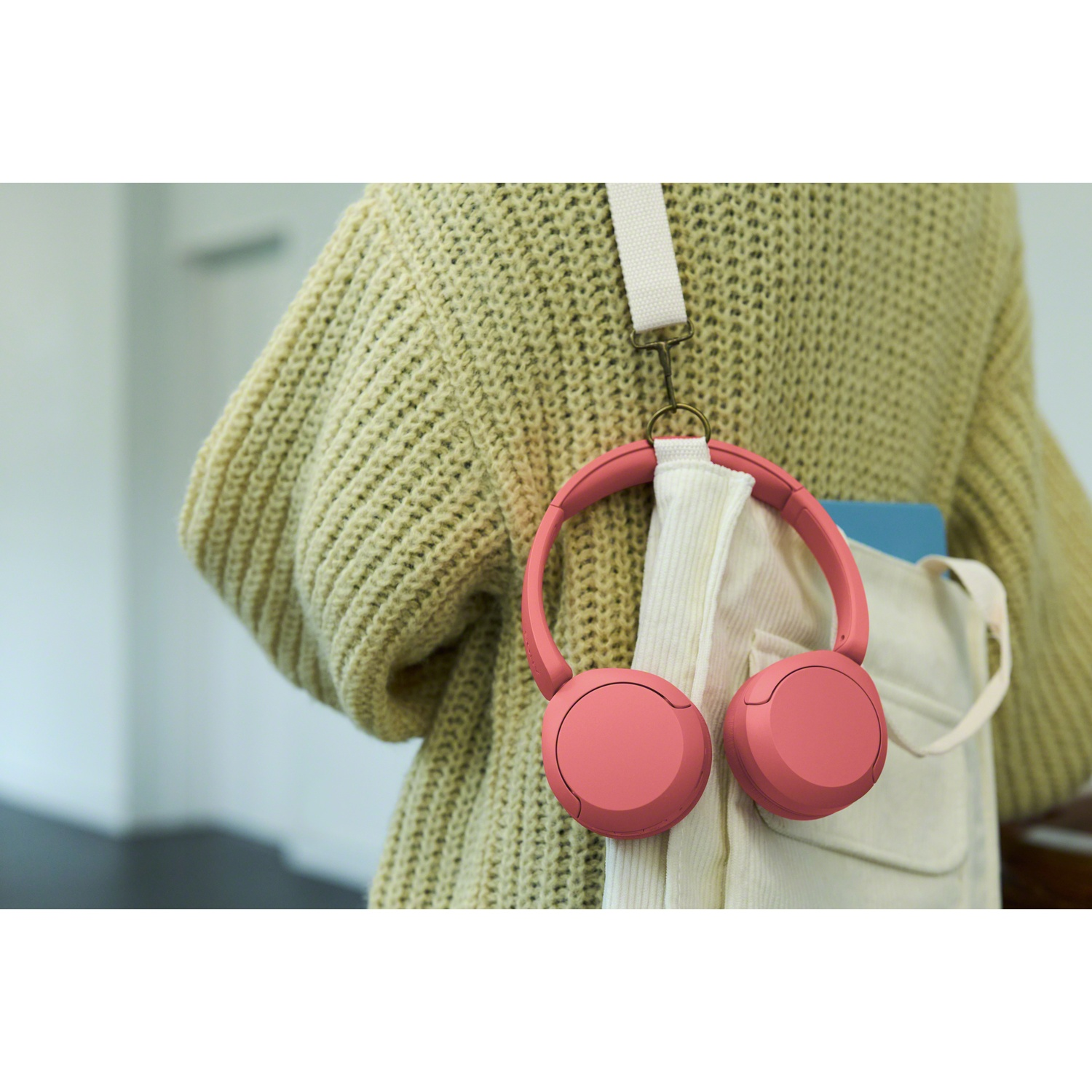 Un casque rose pend à un sac blanc, porté par une personne en pull jaune.