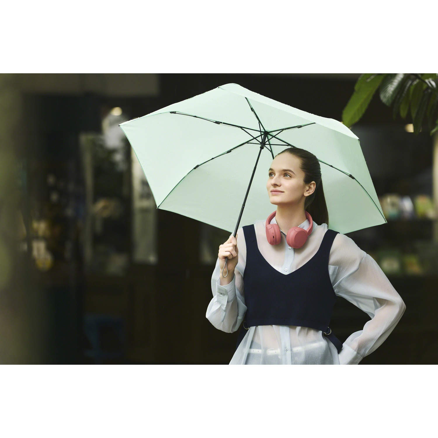 Une femme tient un parapluie vert clair et porte des écouteurs roses.