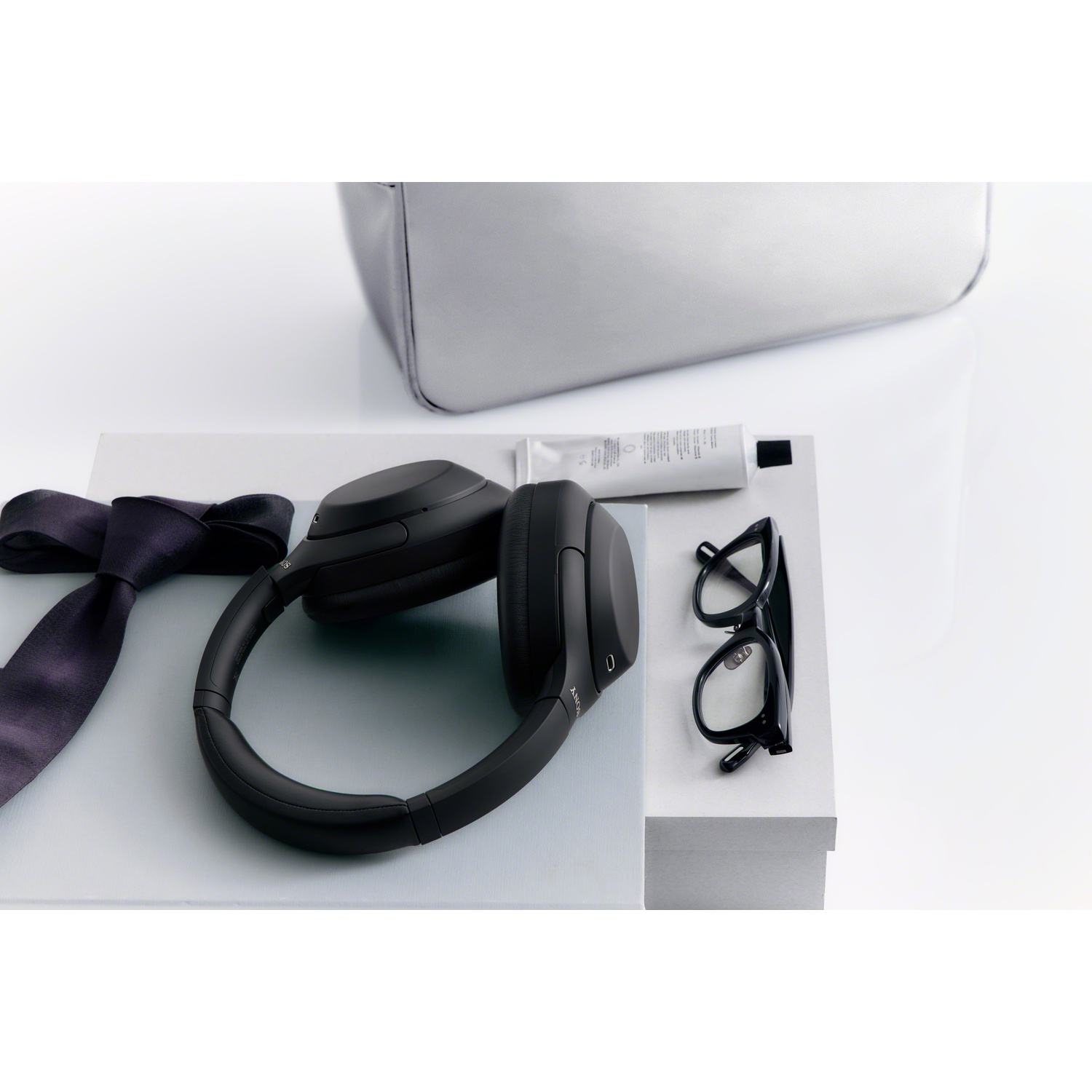 Un casque noir, des lunettes, une cravate et un tube de crème sur des boîtes grises sur fond blanc.