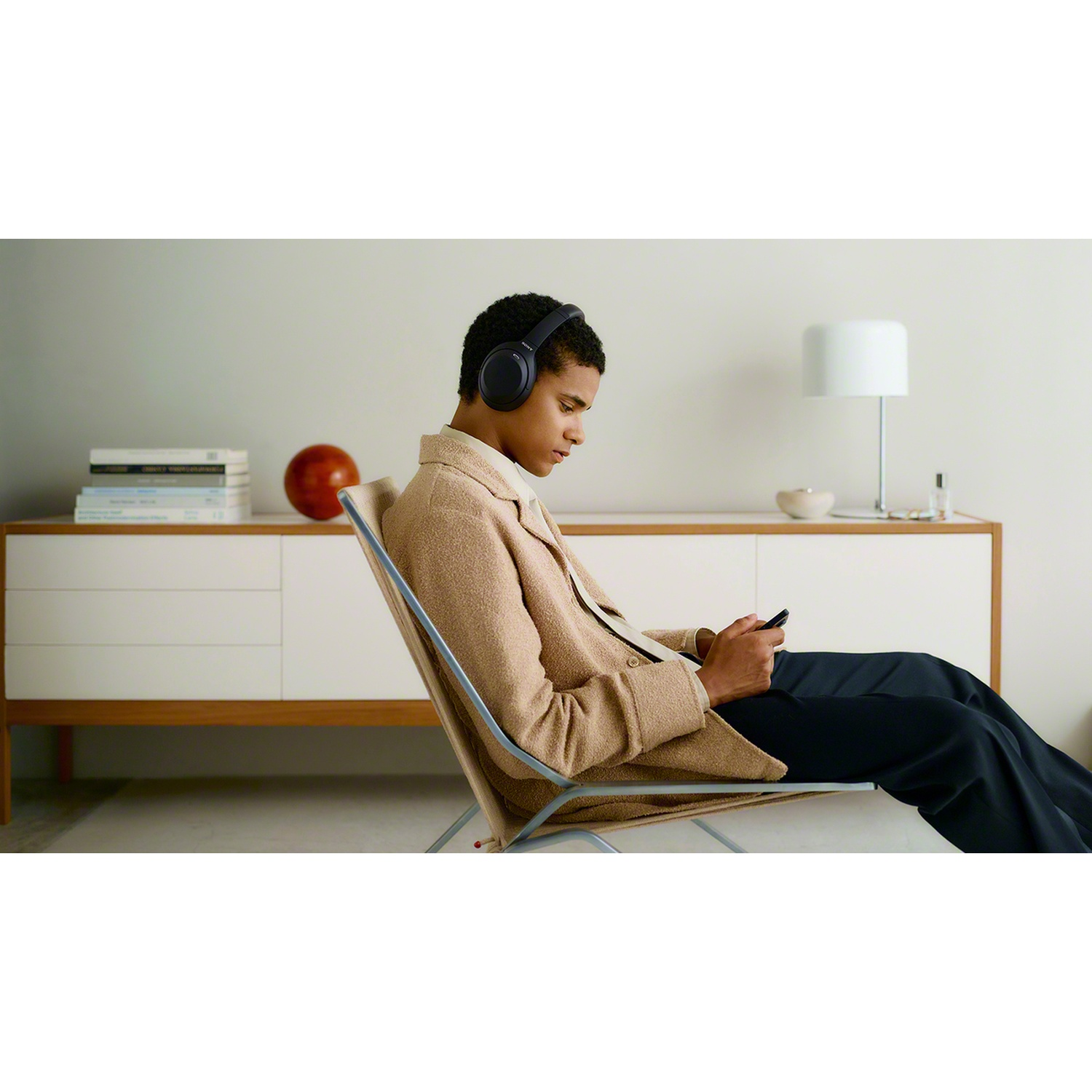 Un jeune homme est assis dans un fauteuil, porte un casque et regarde son smartphone.
