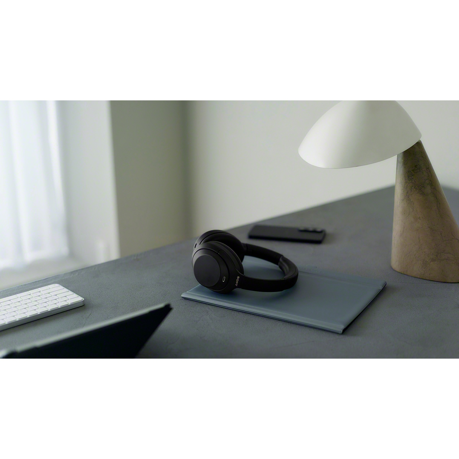 Un casque noir repose sur un bureau gris à côté d'une lampe, d'un smartphone et d'un clavier.