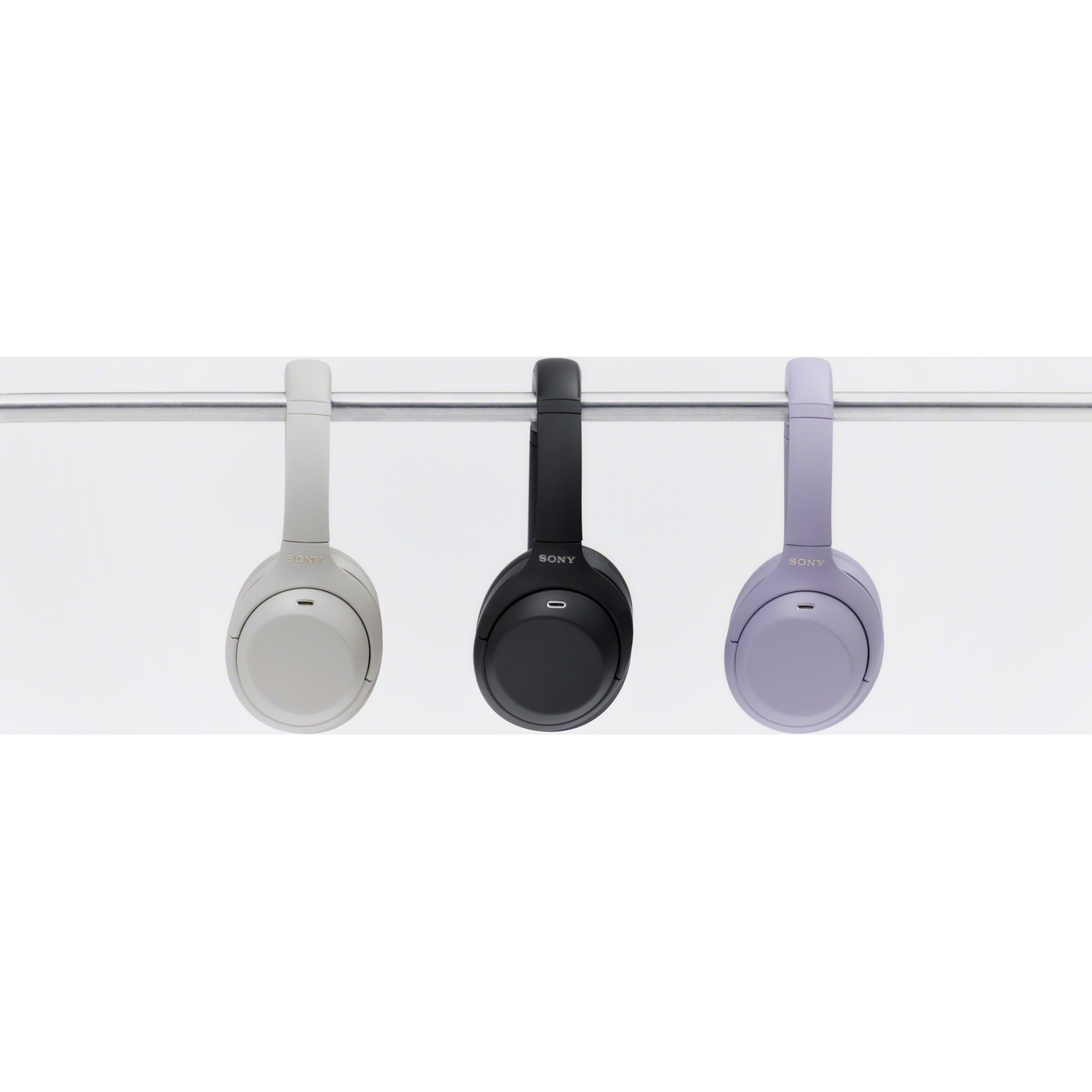 Trois casques Sony beige, noir et violet pendent à une barre métallique sur fond blanc.