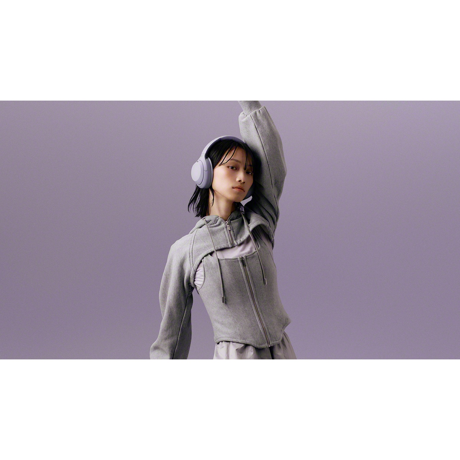 Une femme en vêtements gris porte un casque gris sur un fond violet.