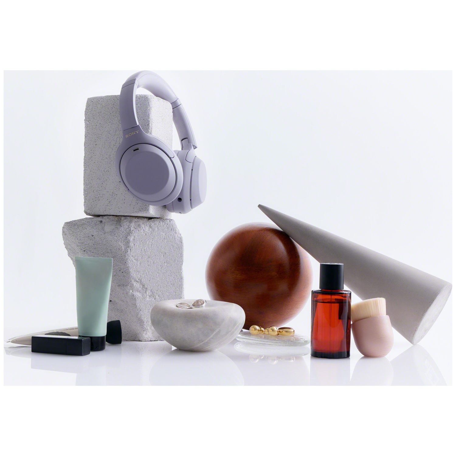 Casque violet sur des blocs de béton, entouré de cosmétiques, de formes arrondies et de bijoux.